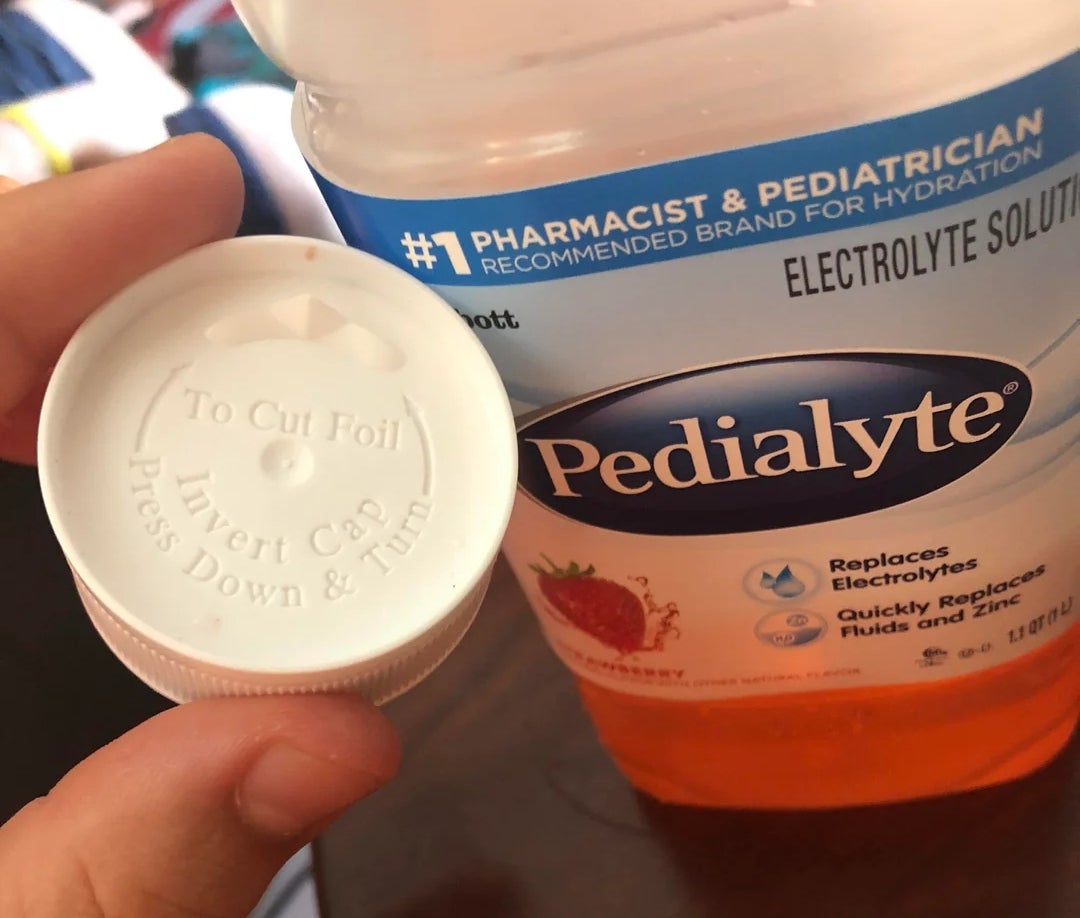 Hånden holder en Pedialyte-flaskekork ved siden av flasken
