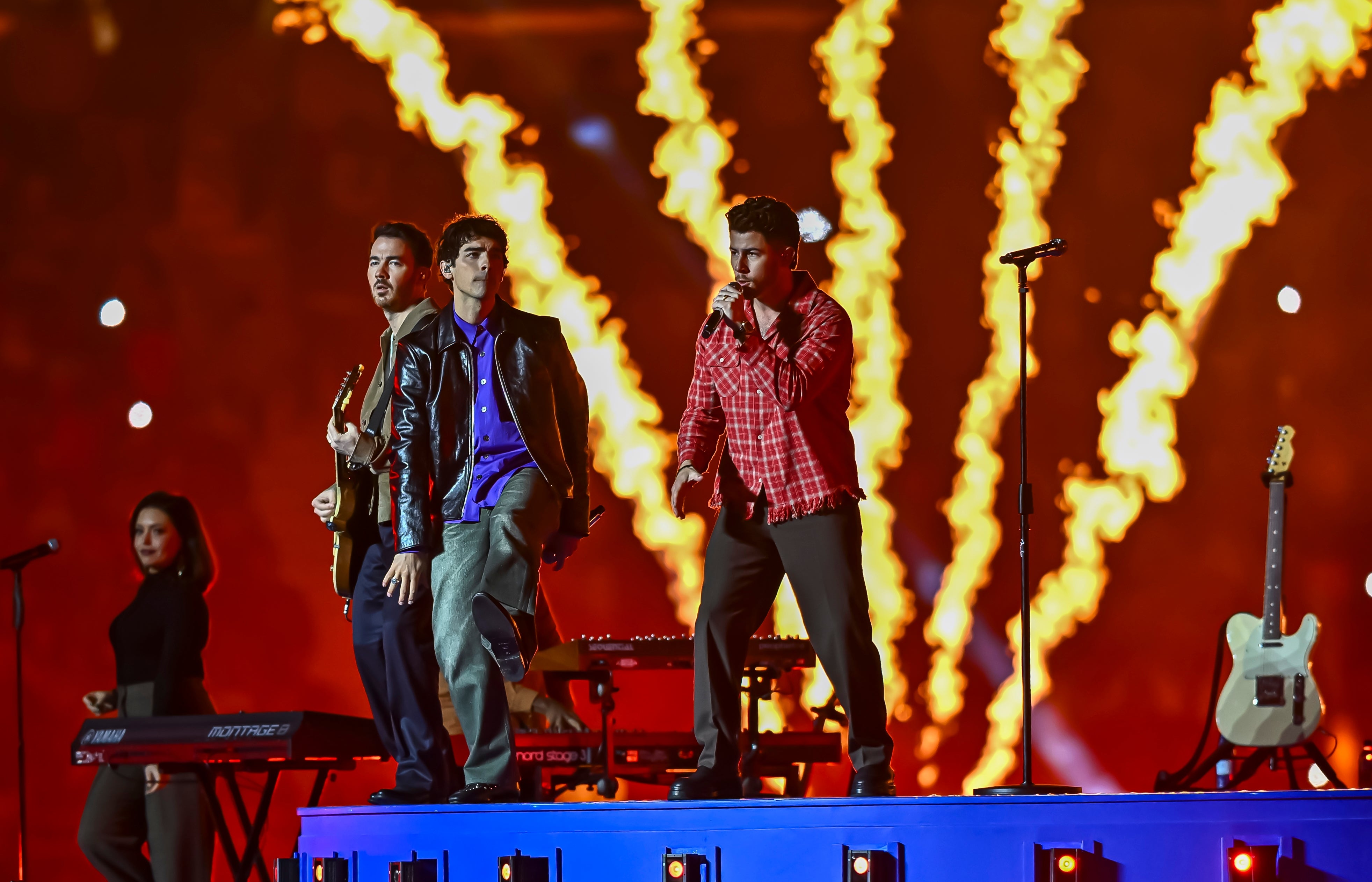 Band performing energetically on stage with flames in the background and a musician playing guitar