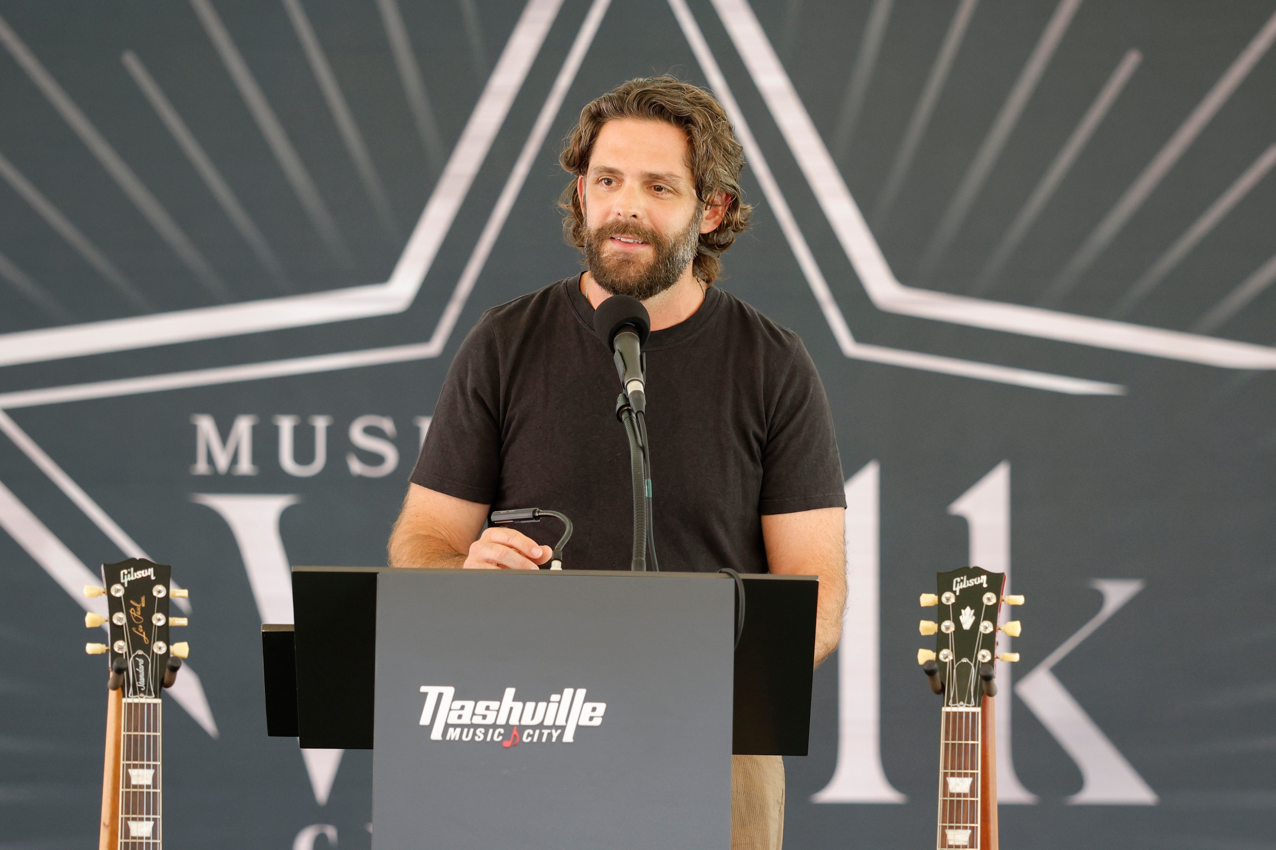 Person speaking at a podium for a Nashville music event with guitars on display nearby