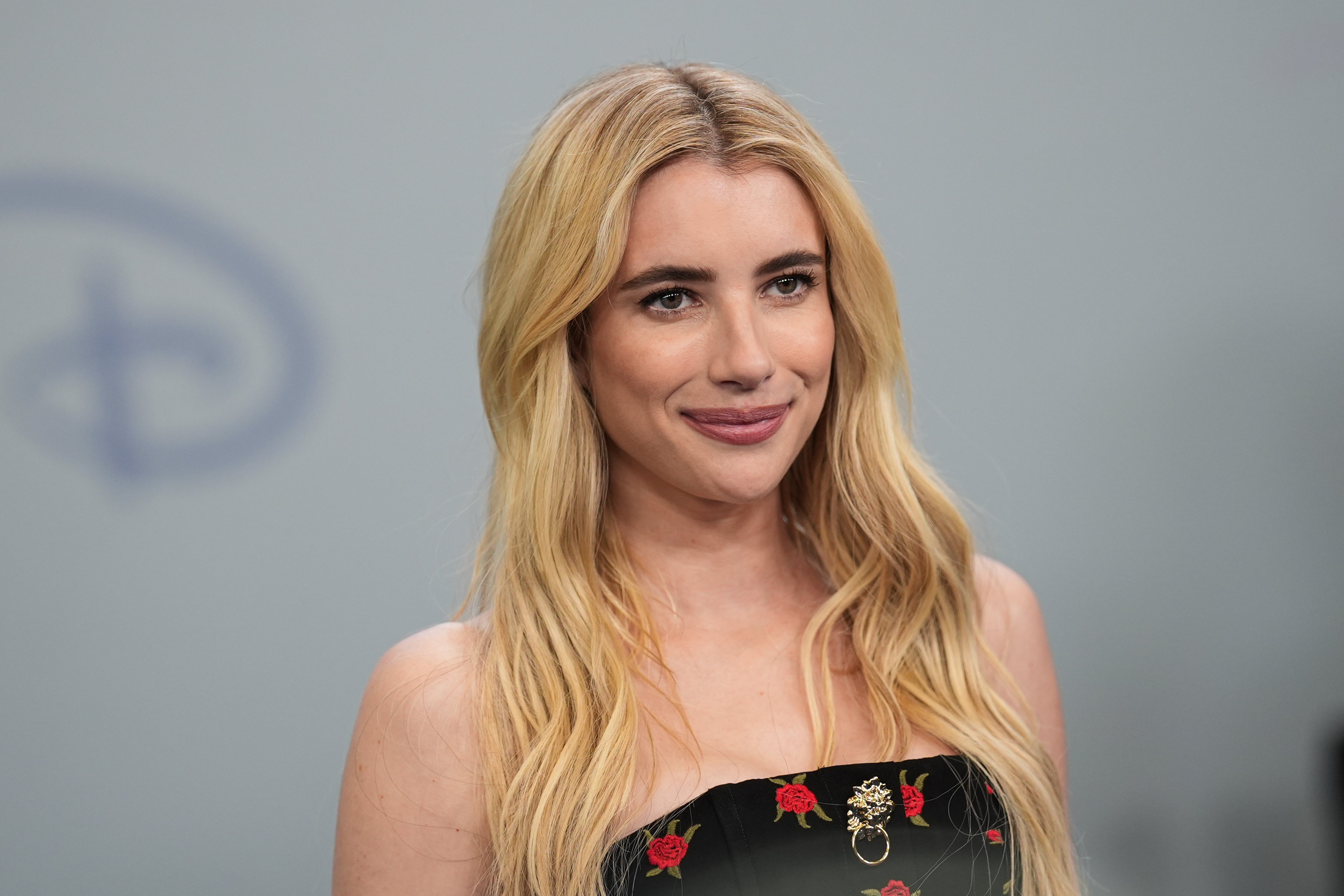 Celebrity in a strapless floral dress, smiling at an event with wavy hair