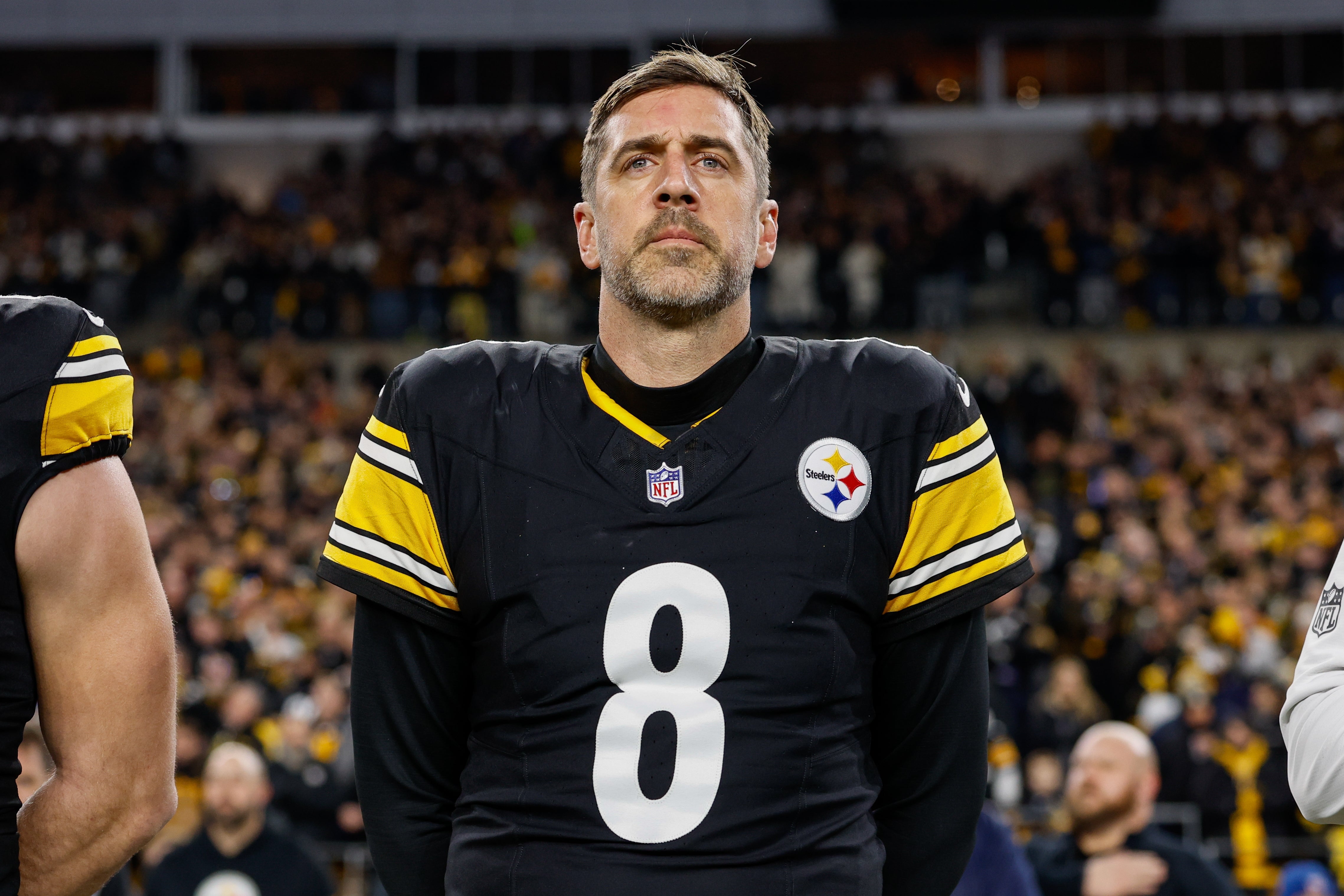 A football player stands on a field wearing a Steelers jersey, looking forward with a serious expression