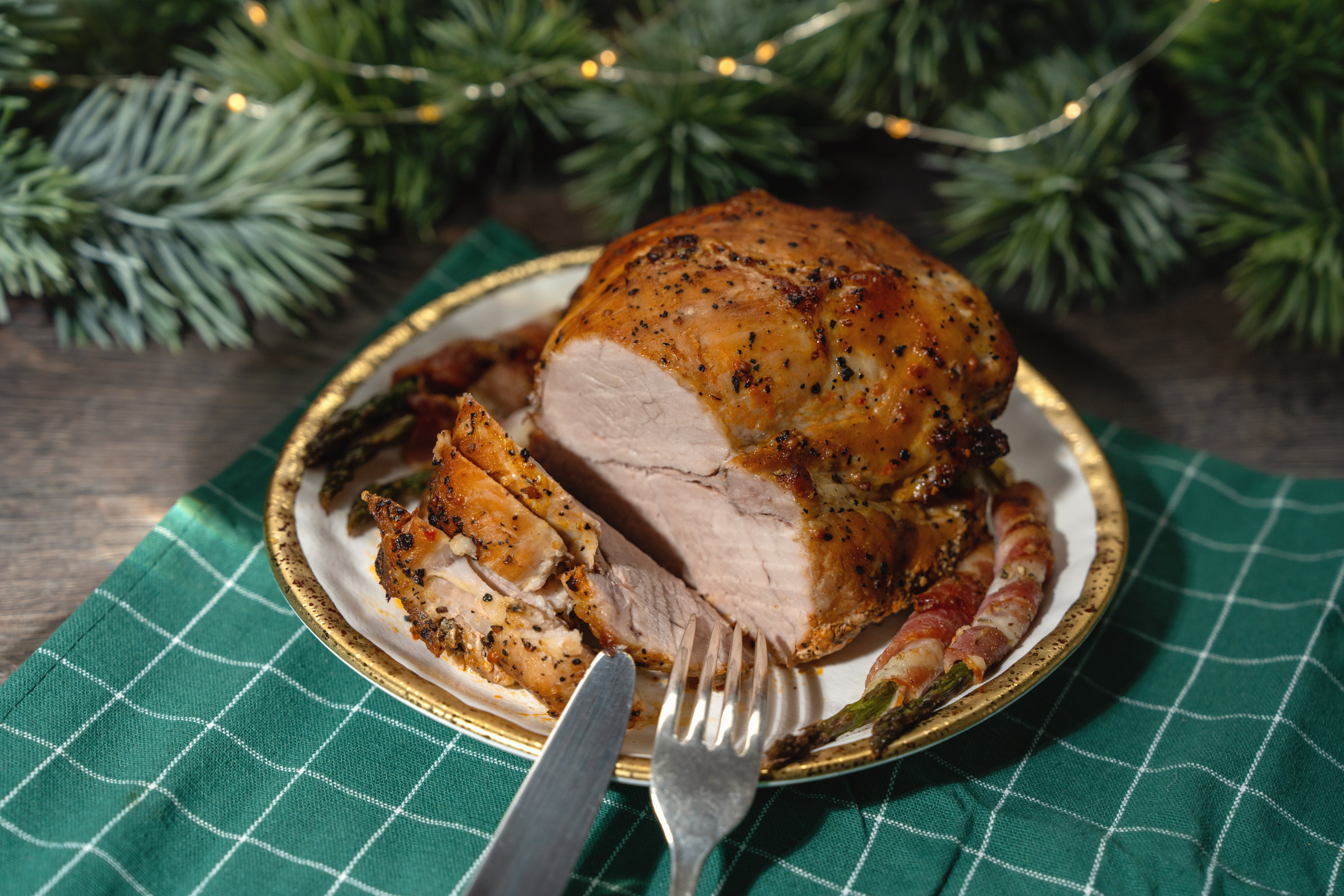 A roasted pork crockery connected a sheet with a portion chopped out, placed connected a greenish checkered cloth, with festive greenery successful the background
