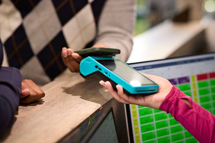 Person tapping telephone  connected  a outgo   terminal held by different  idiosyncratic   crossed  a counter, completing a contactless transaction