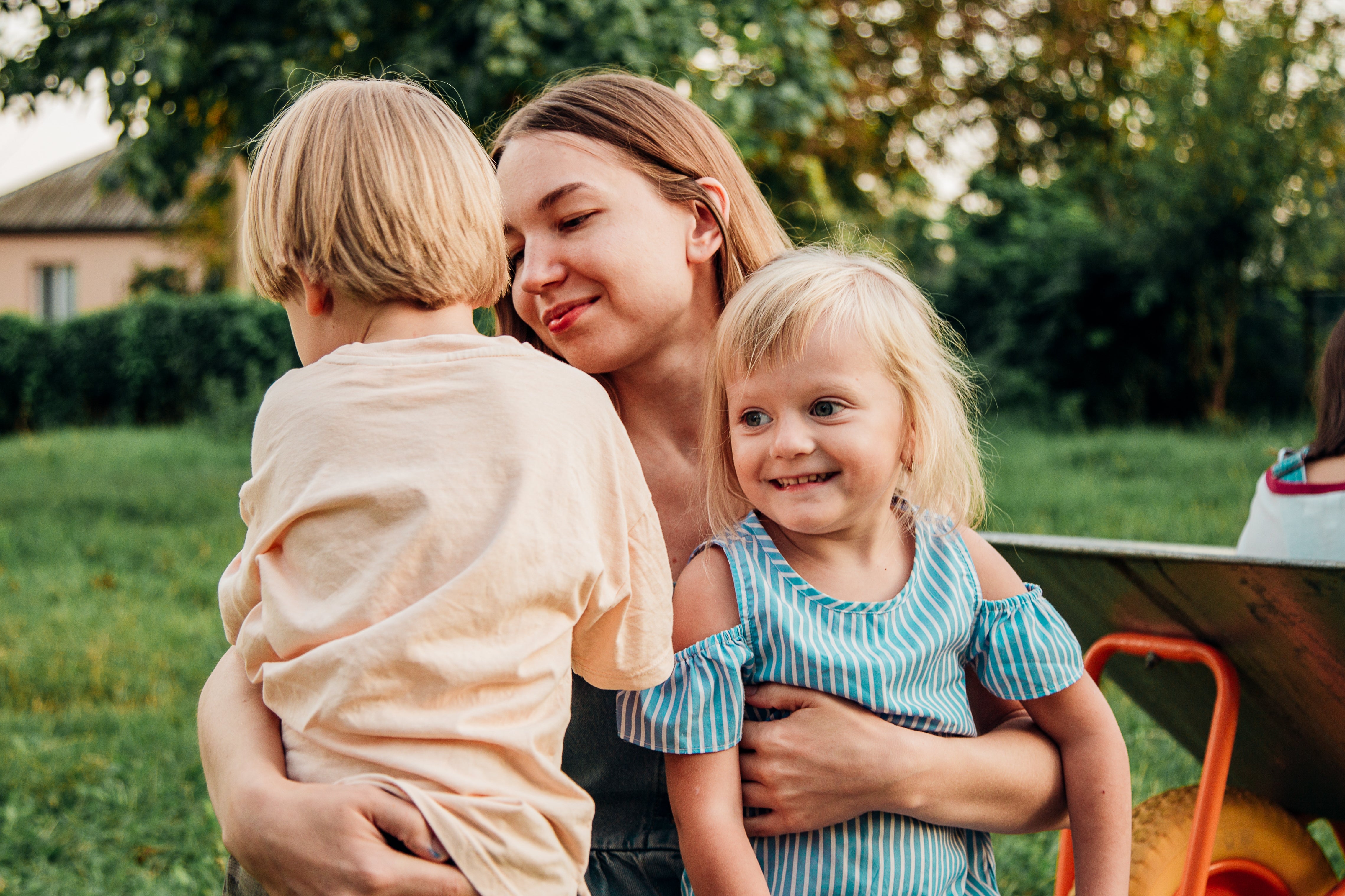 A parent  lovingly embraces her 2  young children outdoors successful  a grassy parkland  setting
