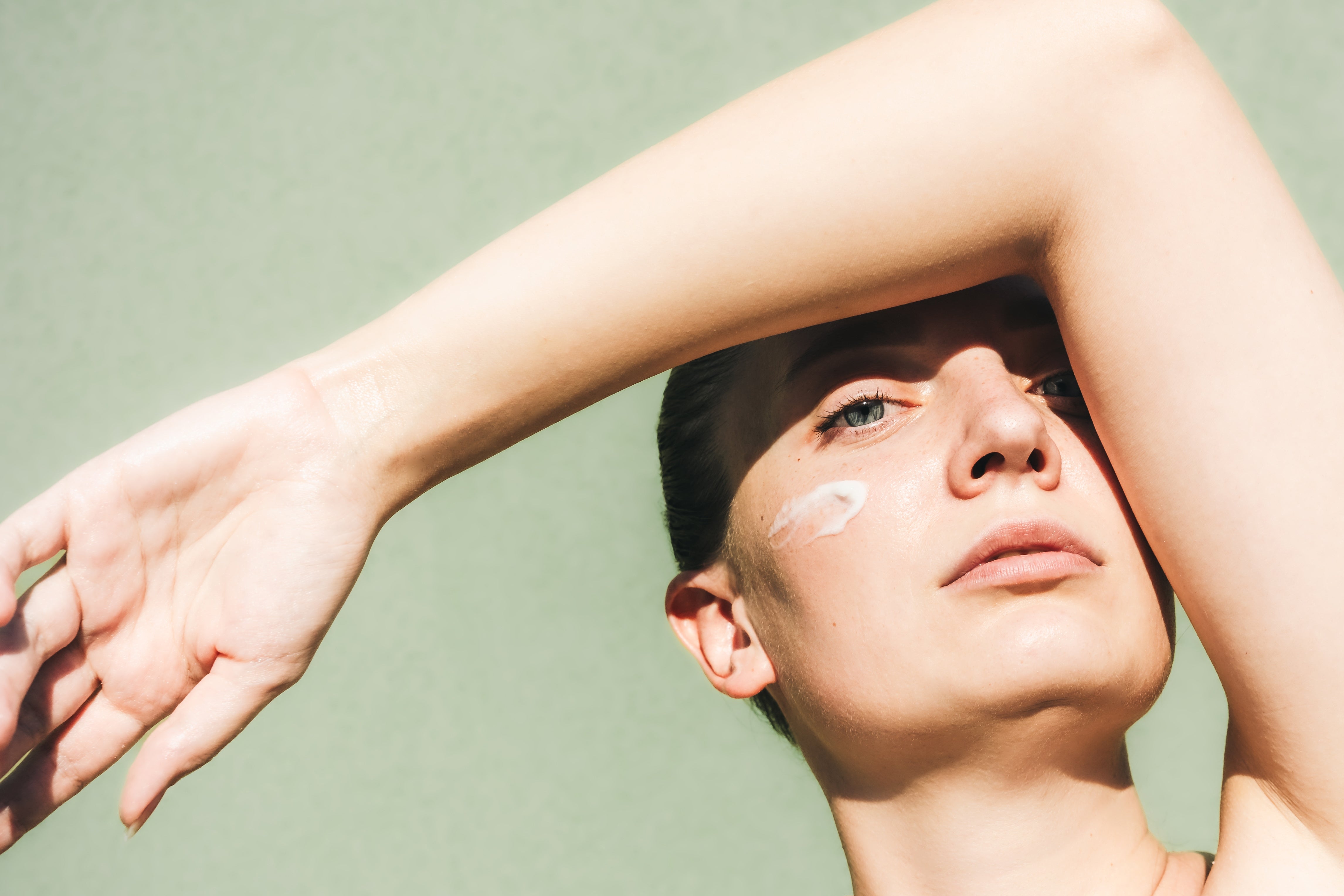 Person with limb  raised, shielding look   partially, looks upwards with a neutral expression; pick  is applied connected  the cheek