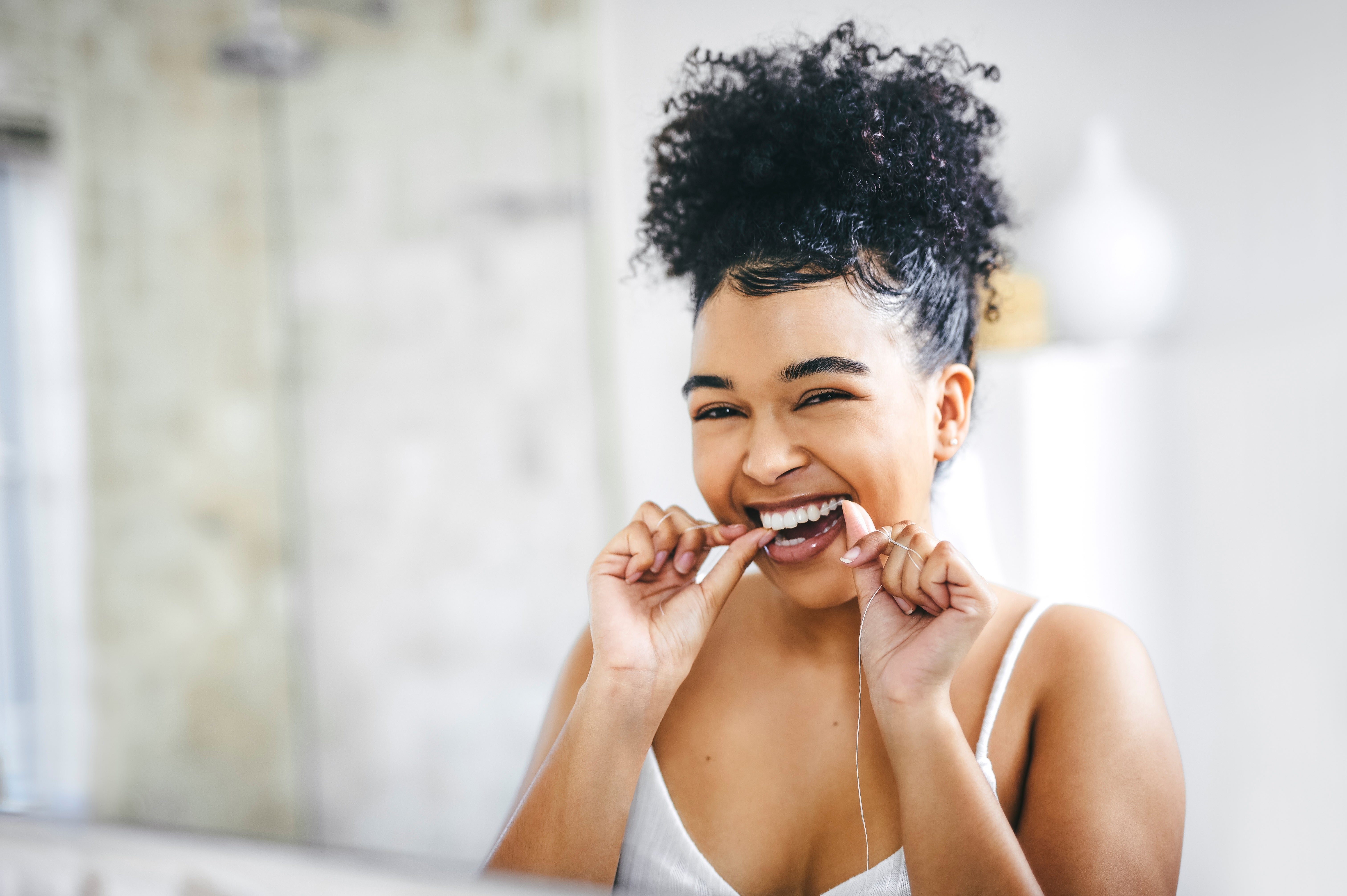 Person smiling portion    flossing their teeth successful  beforehand   of a mirror