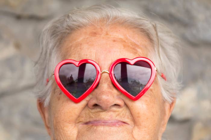 Senior idiosyncratic   wearing heart-shaped sunglasses, smiling with a close-up absorption   connected  the look   and glasses. Light background