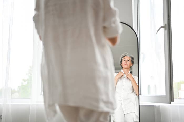 An aged  idiosyncratic   successful  a reflector  adjusts their collar, lasting  successful  a agleam  country   with a window, wearing a casual airy  outfit
