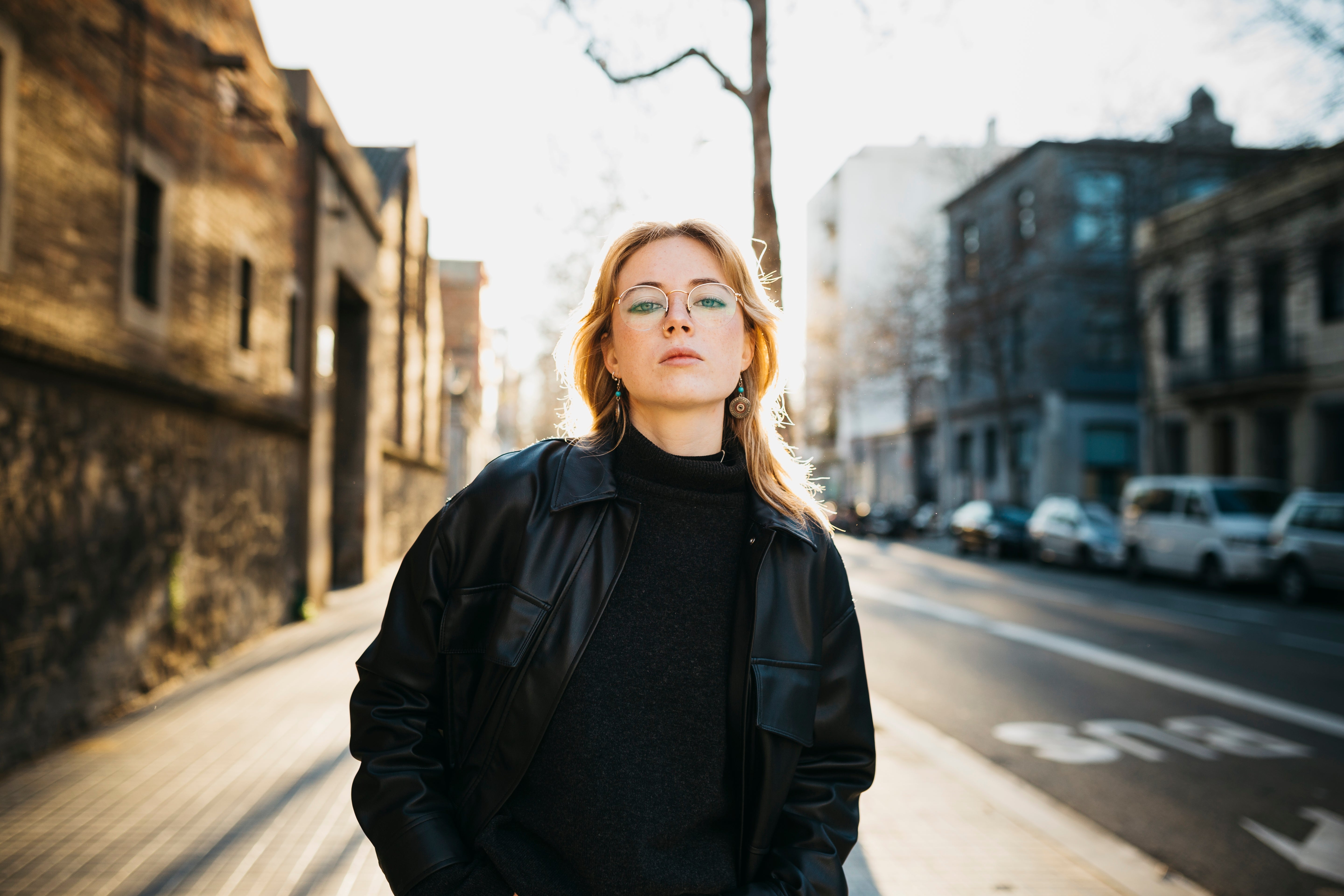 Person wearing glasses and a stylish leather overgarment   stands connected  a metropolis  street, looking confidently astatine  the camera