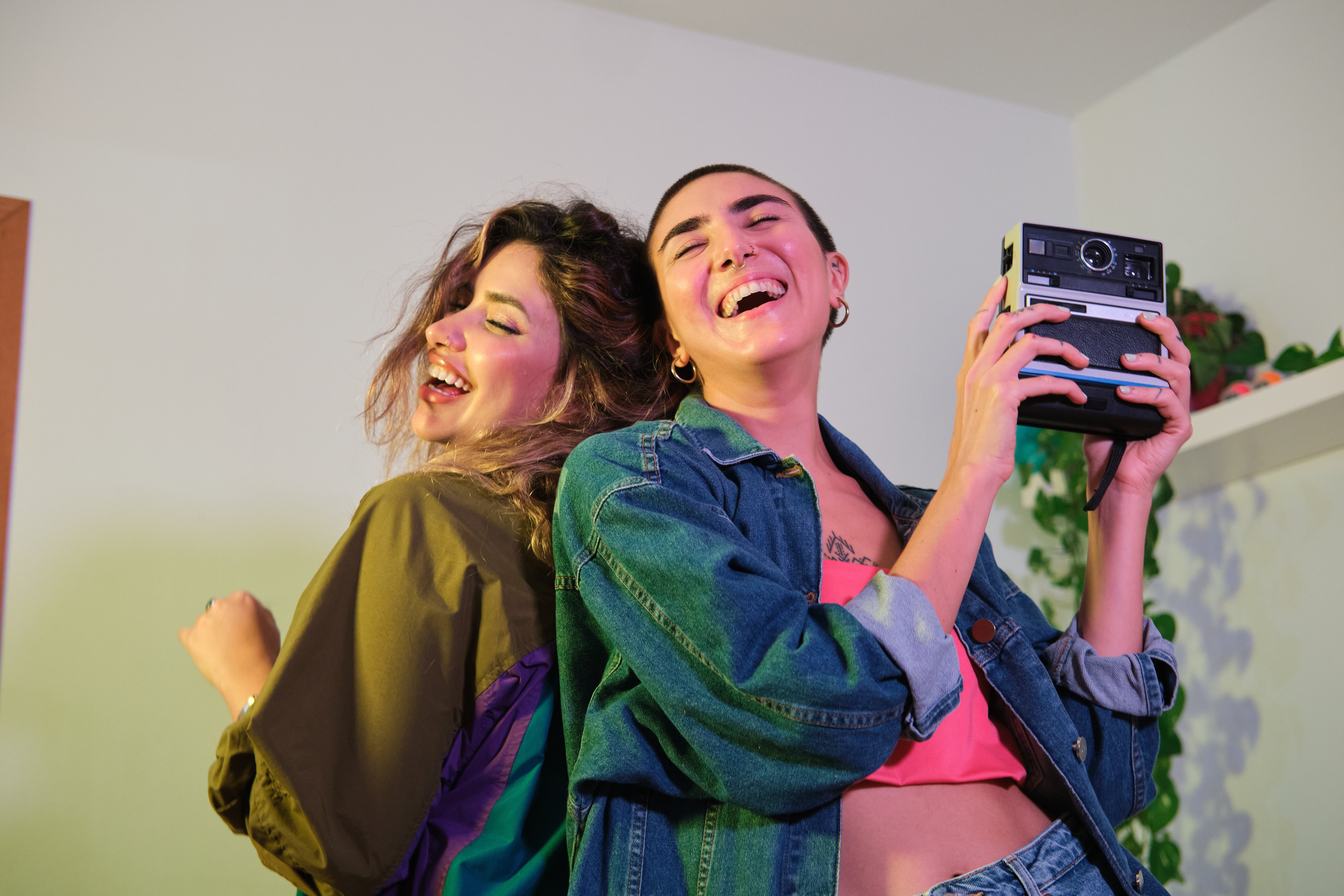 Two radical   smiling and posing with a vintage camera. One wears a casual jacket; the different   has a denim overgarment   implicit    a agleam  top