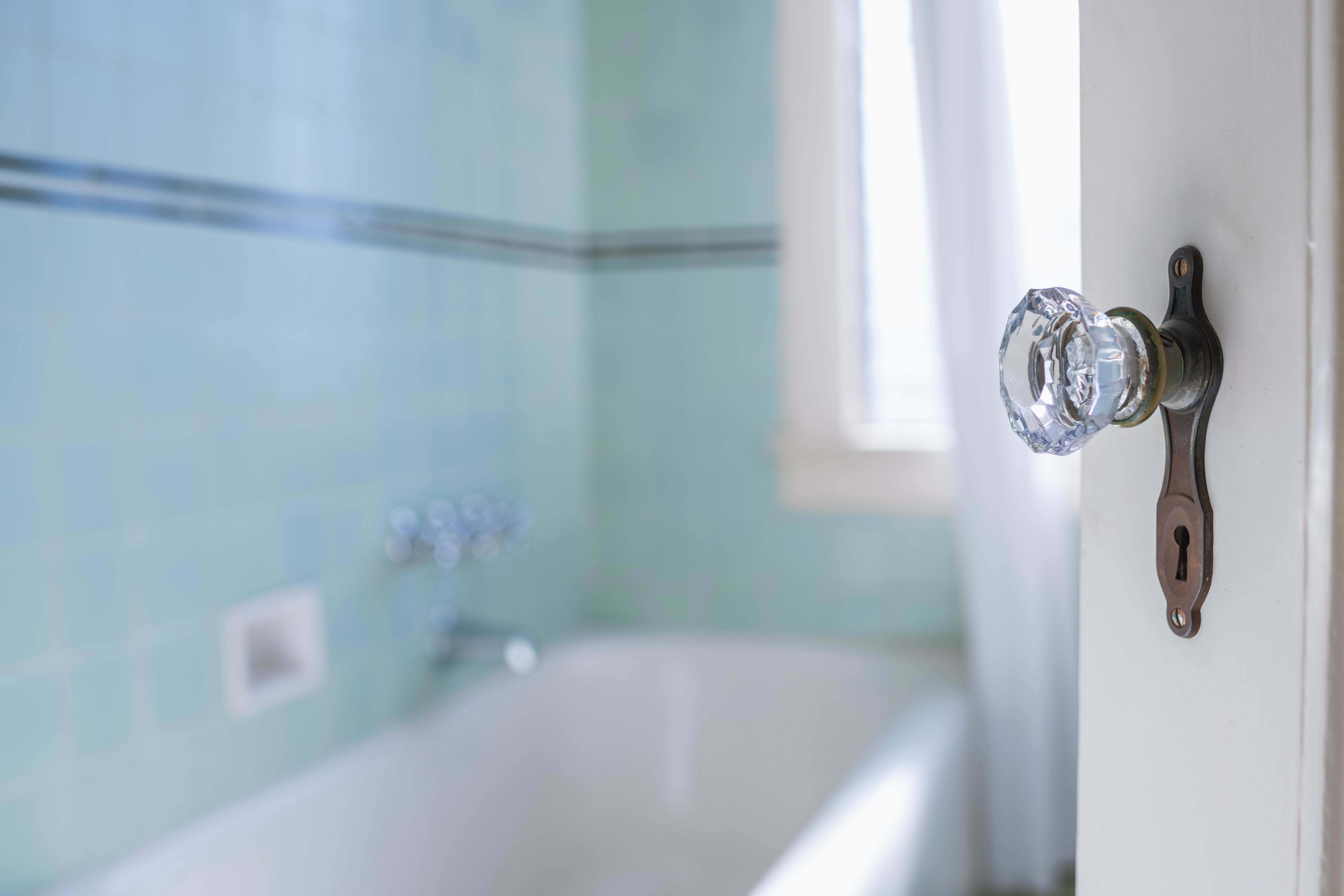 Door with solid knob somewhat open, revealing a tiled bath with a bathtub disposable successful the background