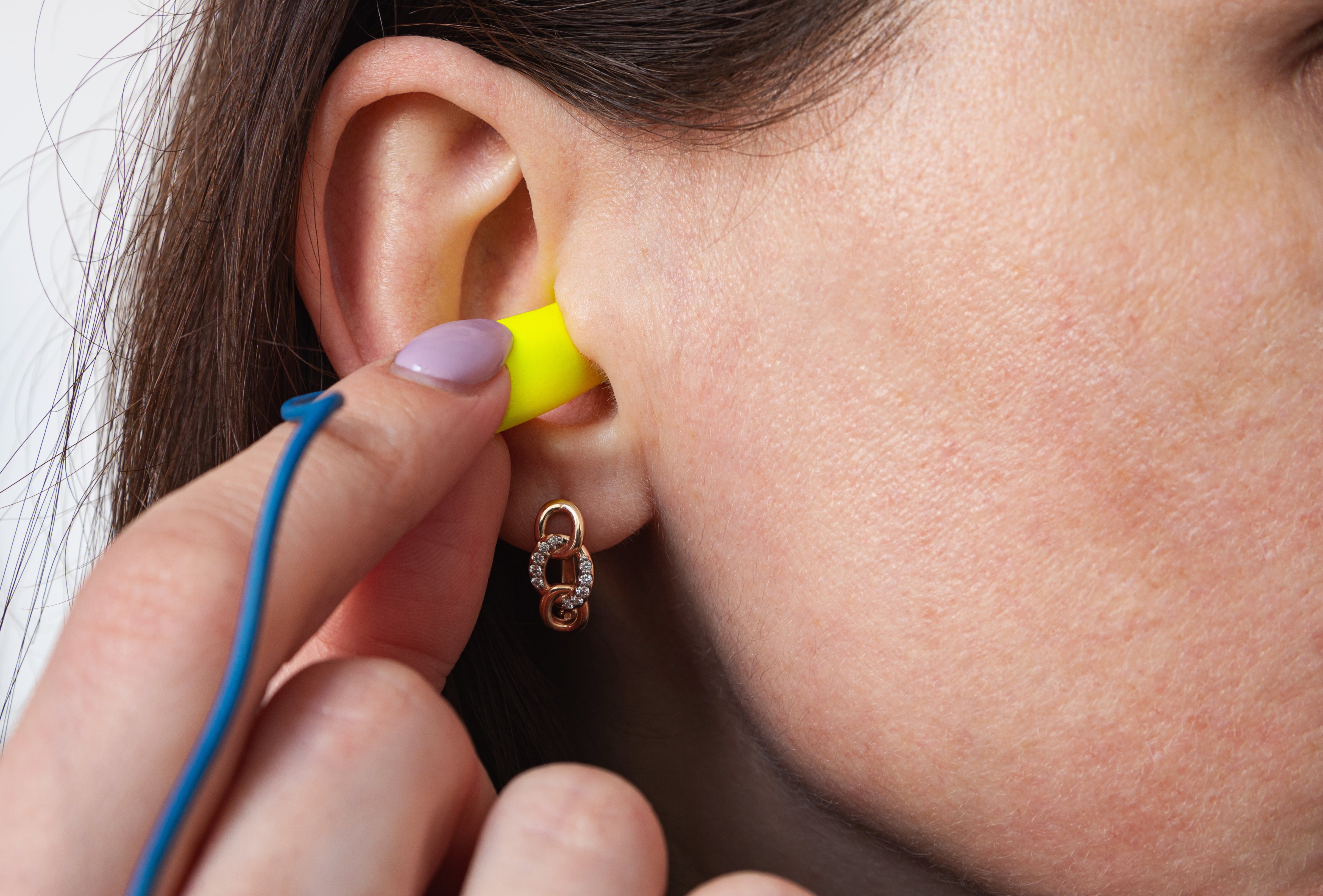 A idiosyncratic   inserts a yellowish  earplug into their ear, wearing a hoop earring