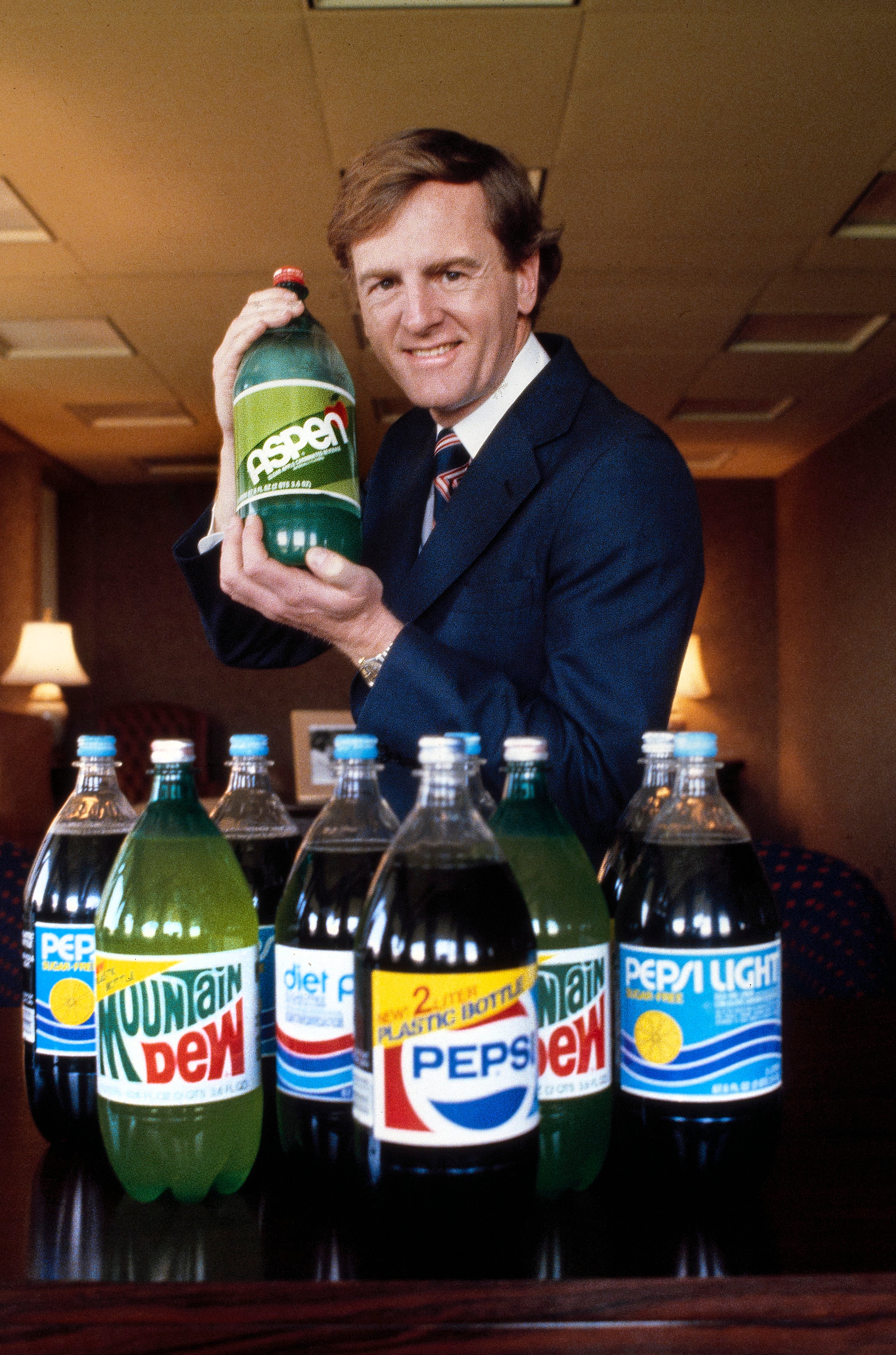 Person successful suit holding a ample vessel of Aspen soda, lasting down a array with assorted brushed portion bottles, including Mountain Dew and Pepsi