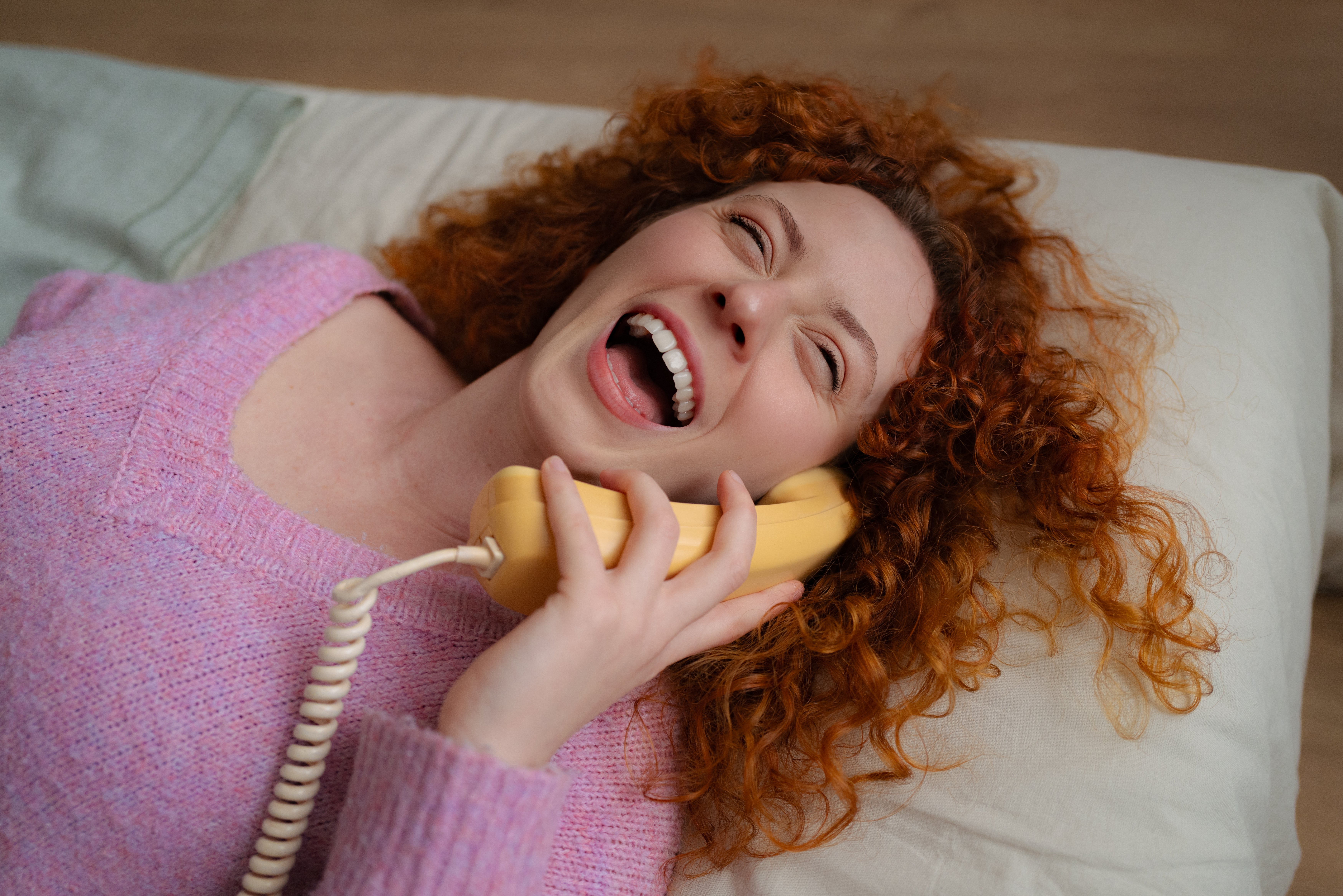 Person with curly hairsbreadth laughing portion talking connected a vintage rotary phone, lying connected a pillow
