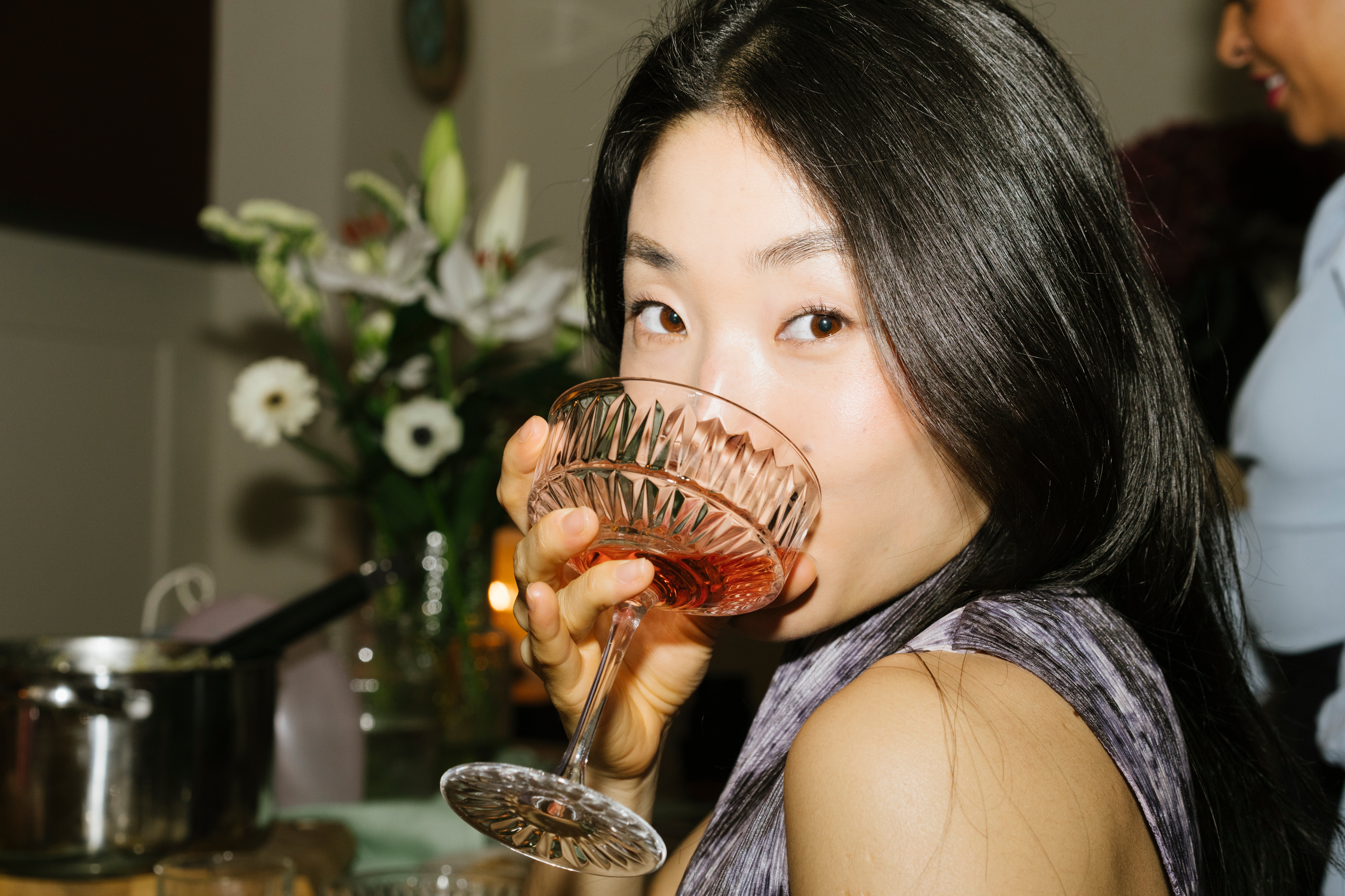 Person sipping from a crystal solid  astatine  a gathering, with flowers and a cookware  successful  the background