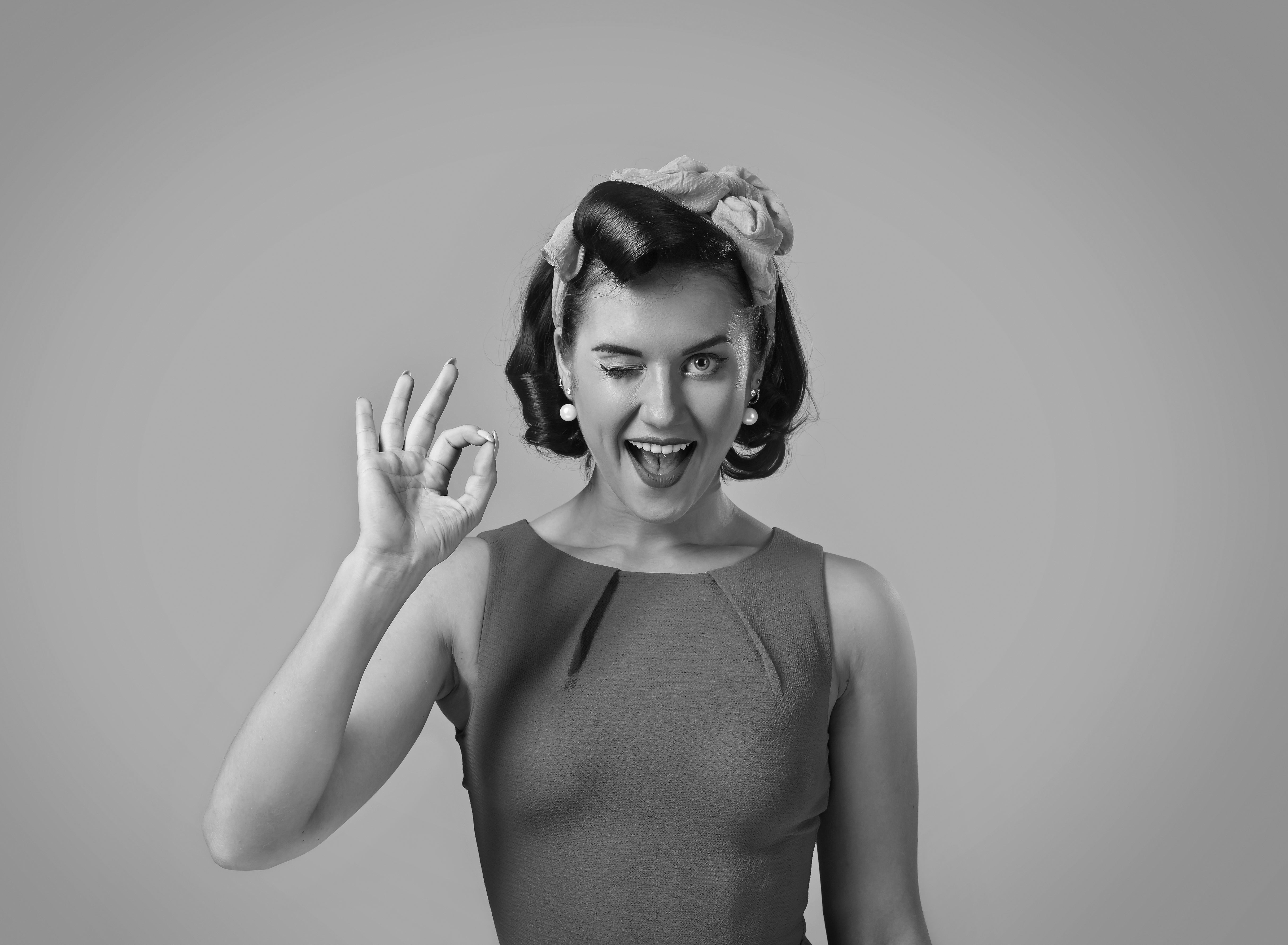 Person successful  vintage attire winks and gestures OK motion   with fingers, expressing playfulness. Hair styled with a headband