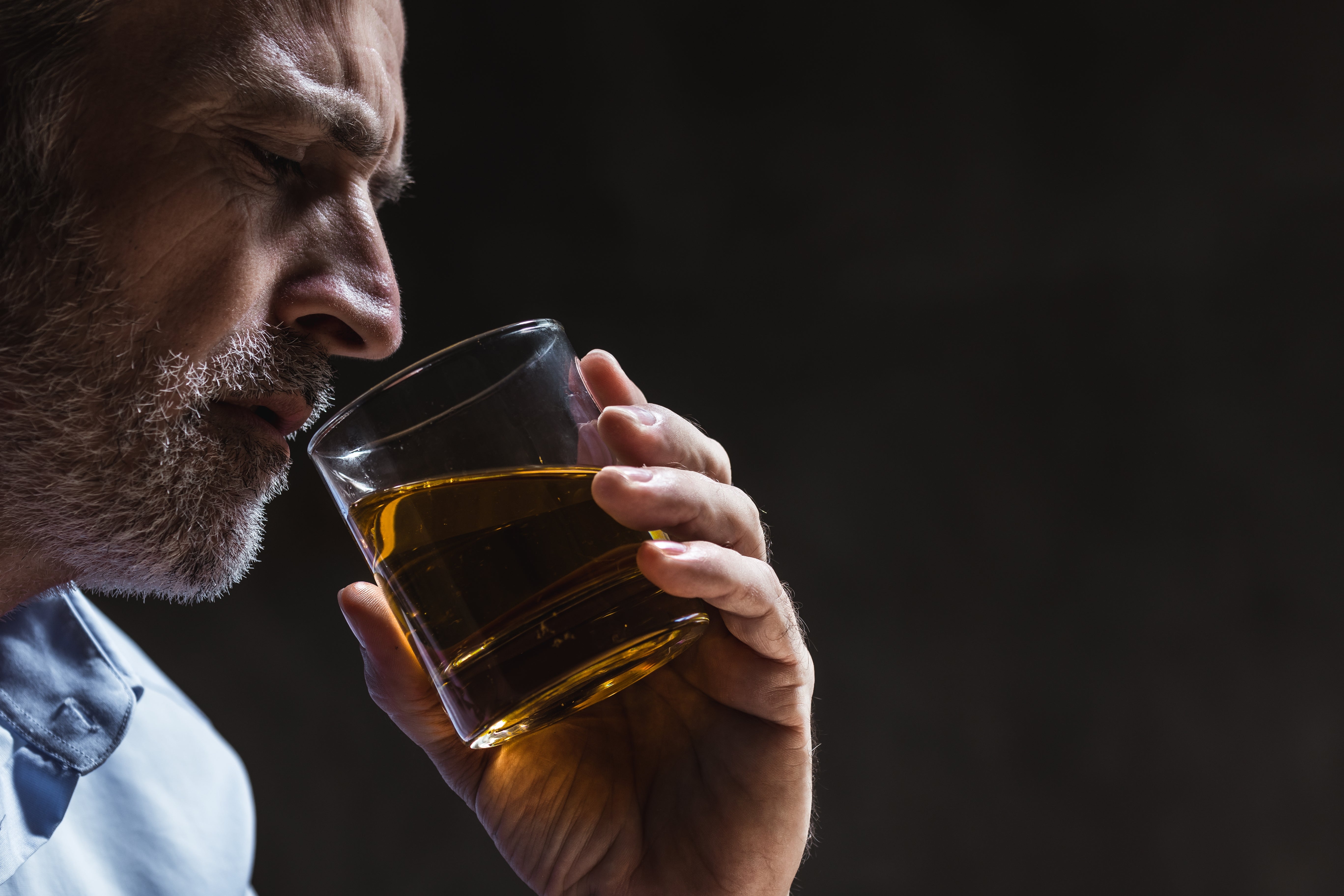 A antheral with a beard holds a solid of whiskey adjacent to his face, appearing contemplative