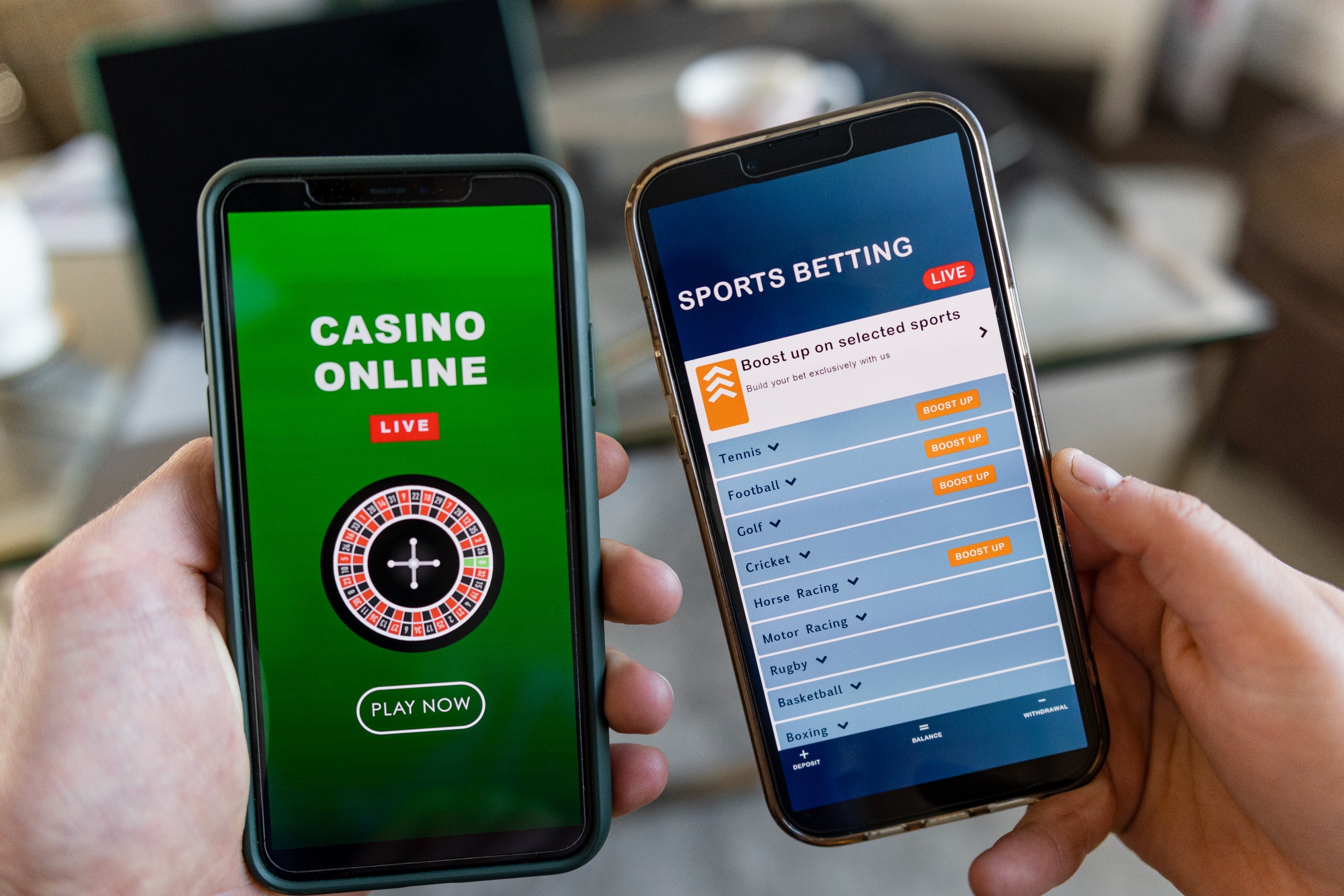 Two smartphones are held broadside by side, displaying a casino app and a sports betting app with unrecorded options