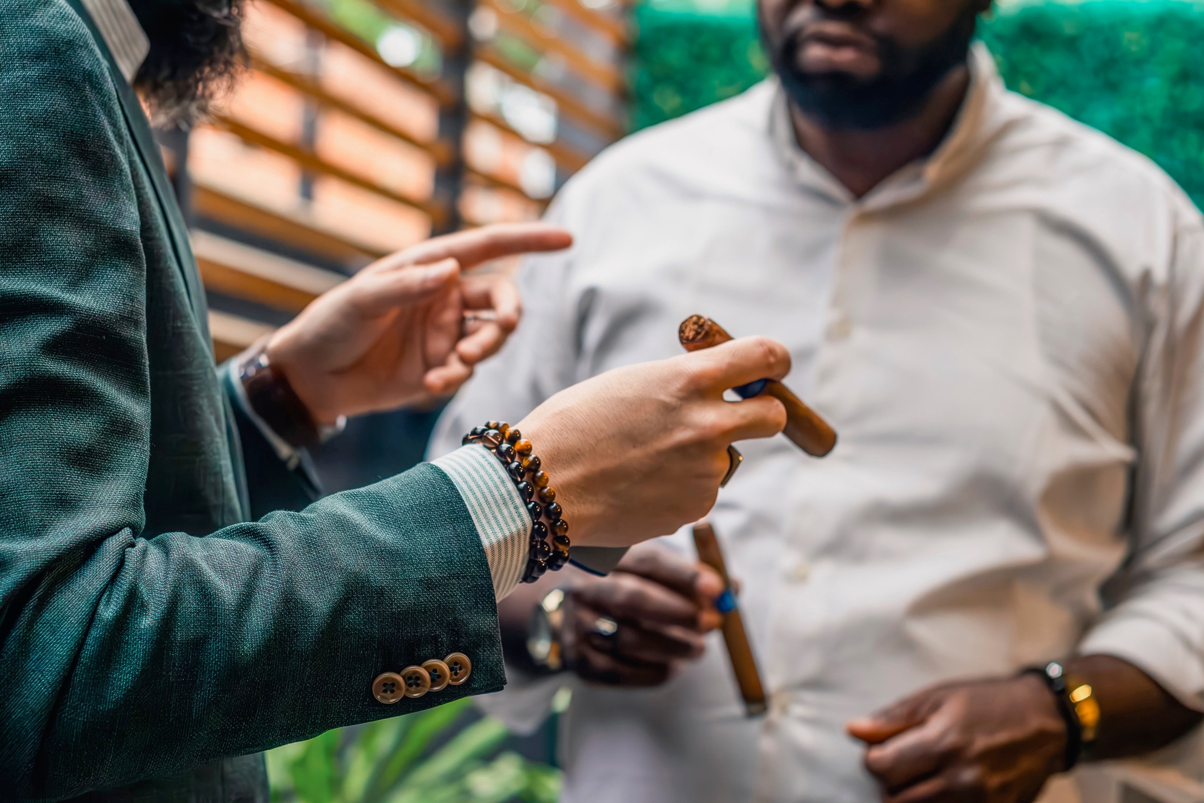 Two radical successful speech holding cigars; 1 gestures with fingers, the different listens, wearing a achromatic garment successful a casual setting
