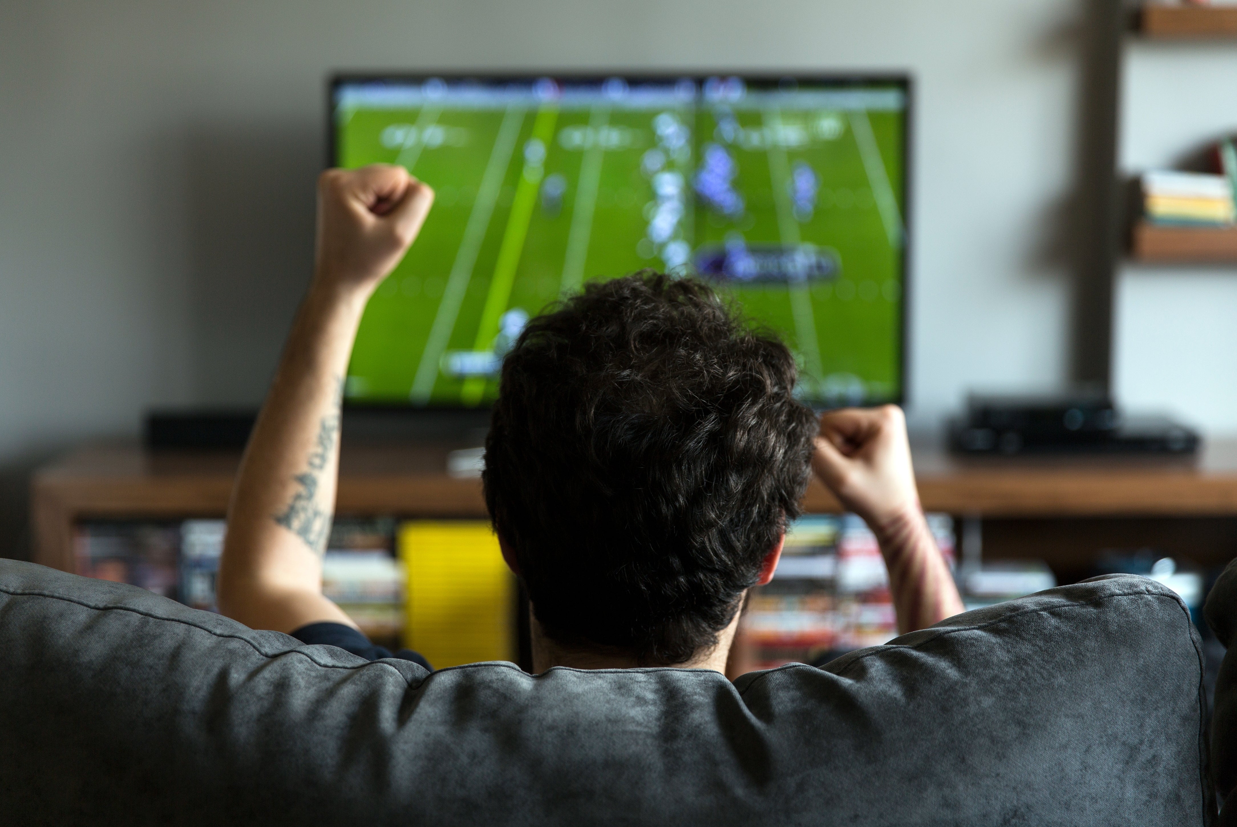 Person sits connected sofa with arms raised, watching a shot crippled connected TV