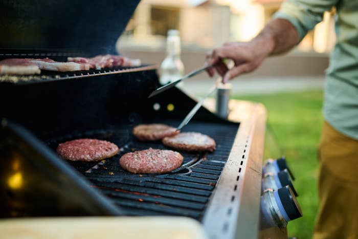 Person grilling burgers connected  an outdoor barbecue, holding tongs. A portion  vessel  is disposable   connected  the side. Relaxed, backyard cookout setting