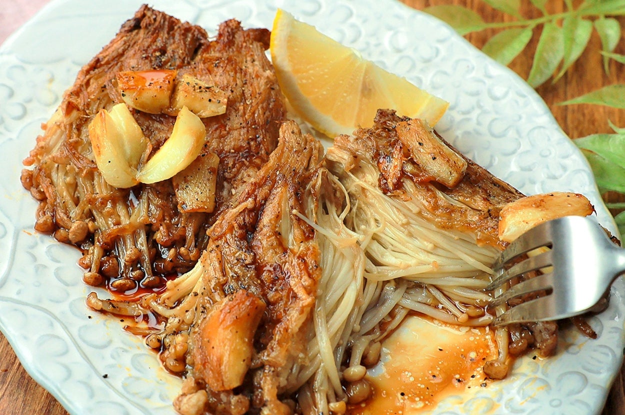 お皿に盛られたエノキと焼き肉がガーリックソースで調理されています。フォークが添えられています。