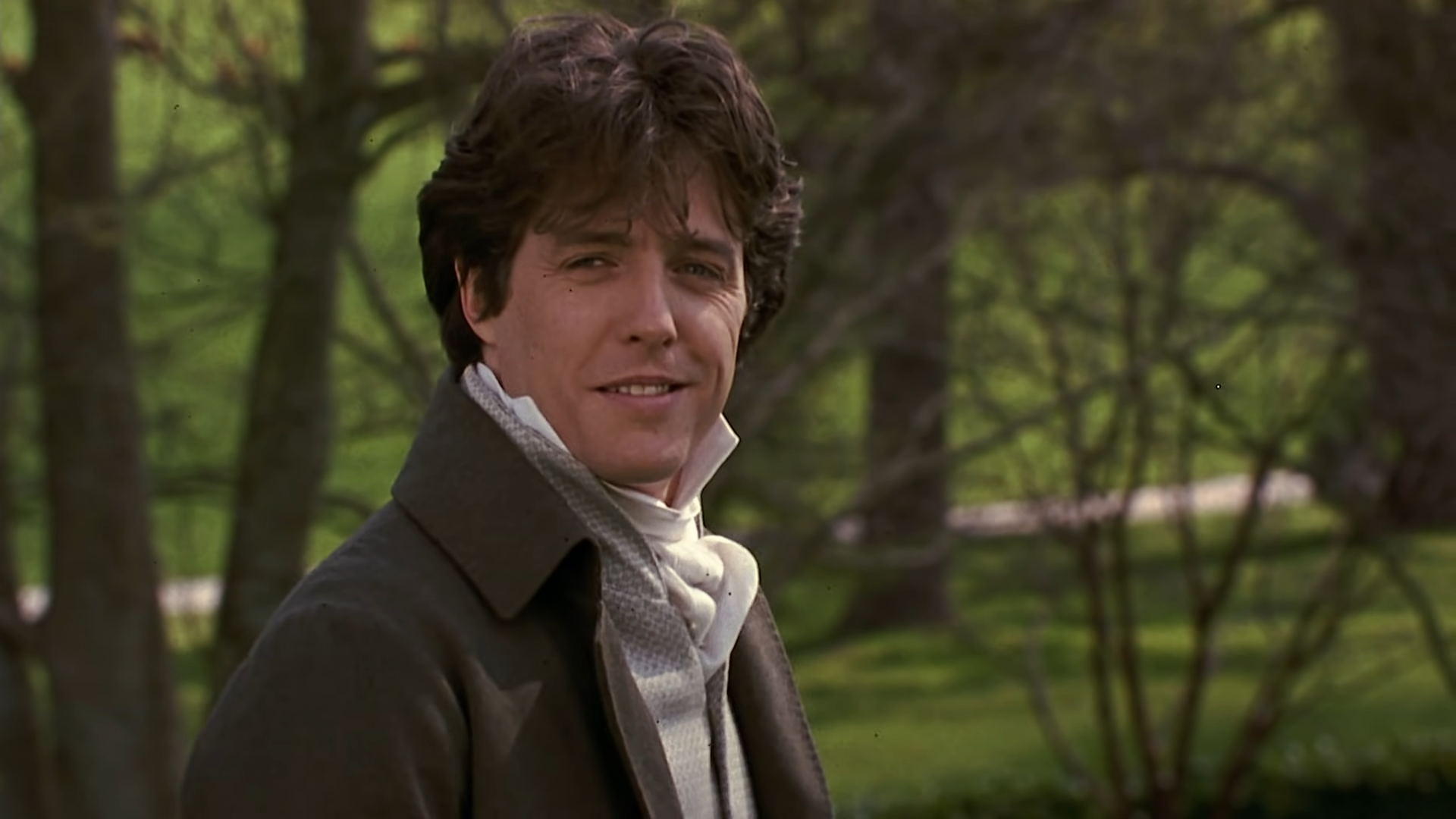 Actor in period-style outfit, featuring a high-collared white shirt and dark coat, set in a lush outdoor environment