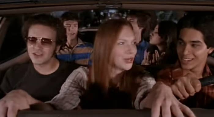 Group of teenagers in a car, smiling and chatting, reminiscent of a scene from a TV show featuring friends on a road trip