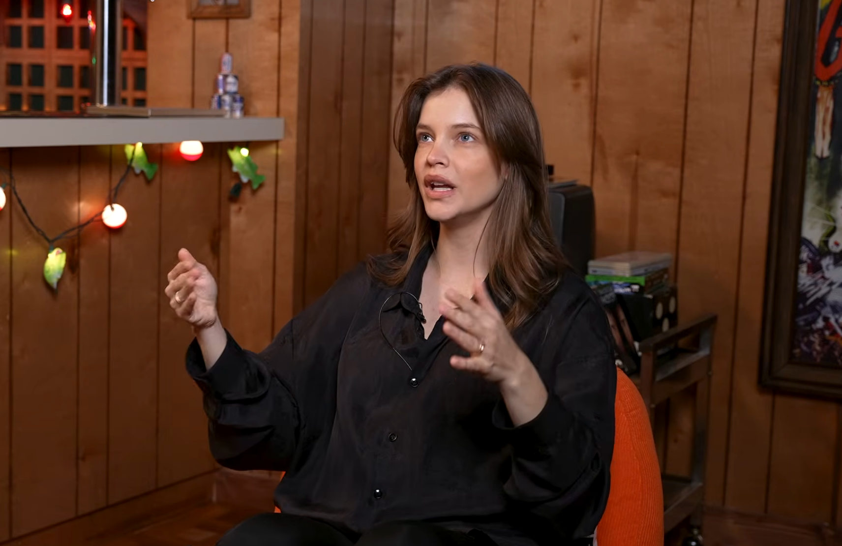 Person in a casual setting, wearing a loose, dark shirt, gesturing while speaking during an interview