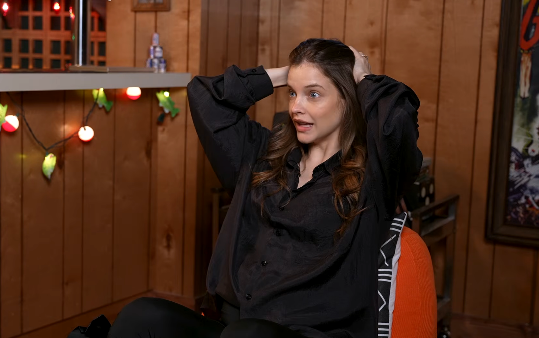 A person in a cozy room, wearing a loose-fitting shirt, looks surprised with hands on their head