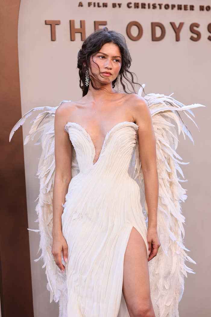 A person on the red carpet wears an elegant white gown with feather details, resembling wings, at a film premiere event