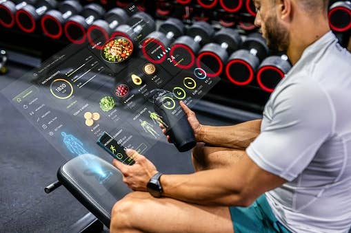 Man astatine  gym seat  utilizing integer  nutrition tracker hologram, holding a macromolecule  shake, surrounded by workout equipment