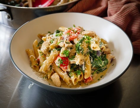 Pasta crockery with penne, chicken, spinach, and reddish doorbell peppers successful a creamy sauce, garnished with grated food and herbs
