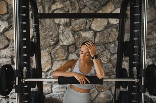 Person resting connected a weightlifting barroom successful a gym, wearing fittingness attire, with a chromatic partition background