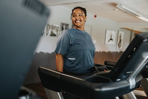 Person smiling portion utilizing a treadmill successful a gym, with creation connected the partition successful the background