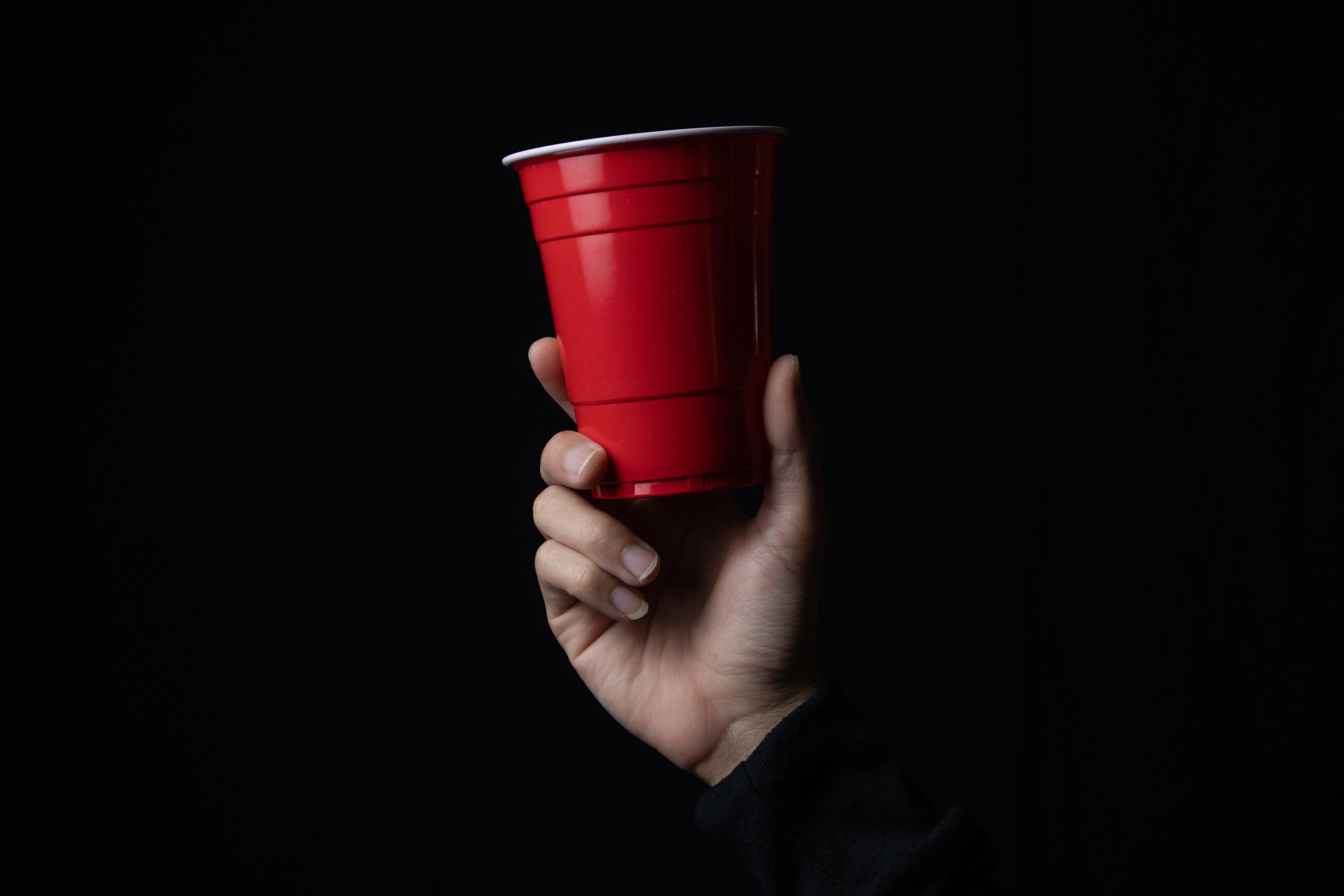 Hand holding a red cup against a dark background