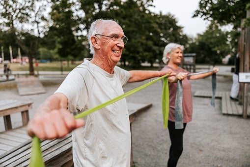 Older adults exercising with absorption bands outdoors, smiling and engaged successful fittingness activity