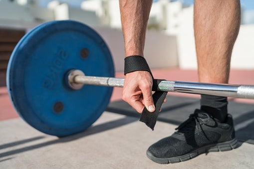 Person wrapping a wrist strap connected a barbell, preparing for weightlifting