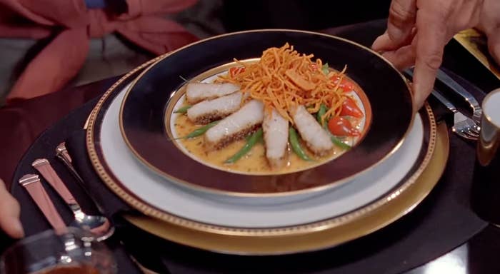 A gourmet dish plated with sliced fish, green beans, cherry tomatoes, and crispy toppings, elegantly presented on a table