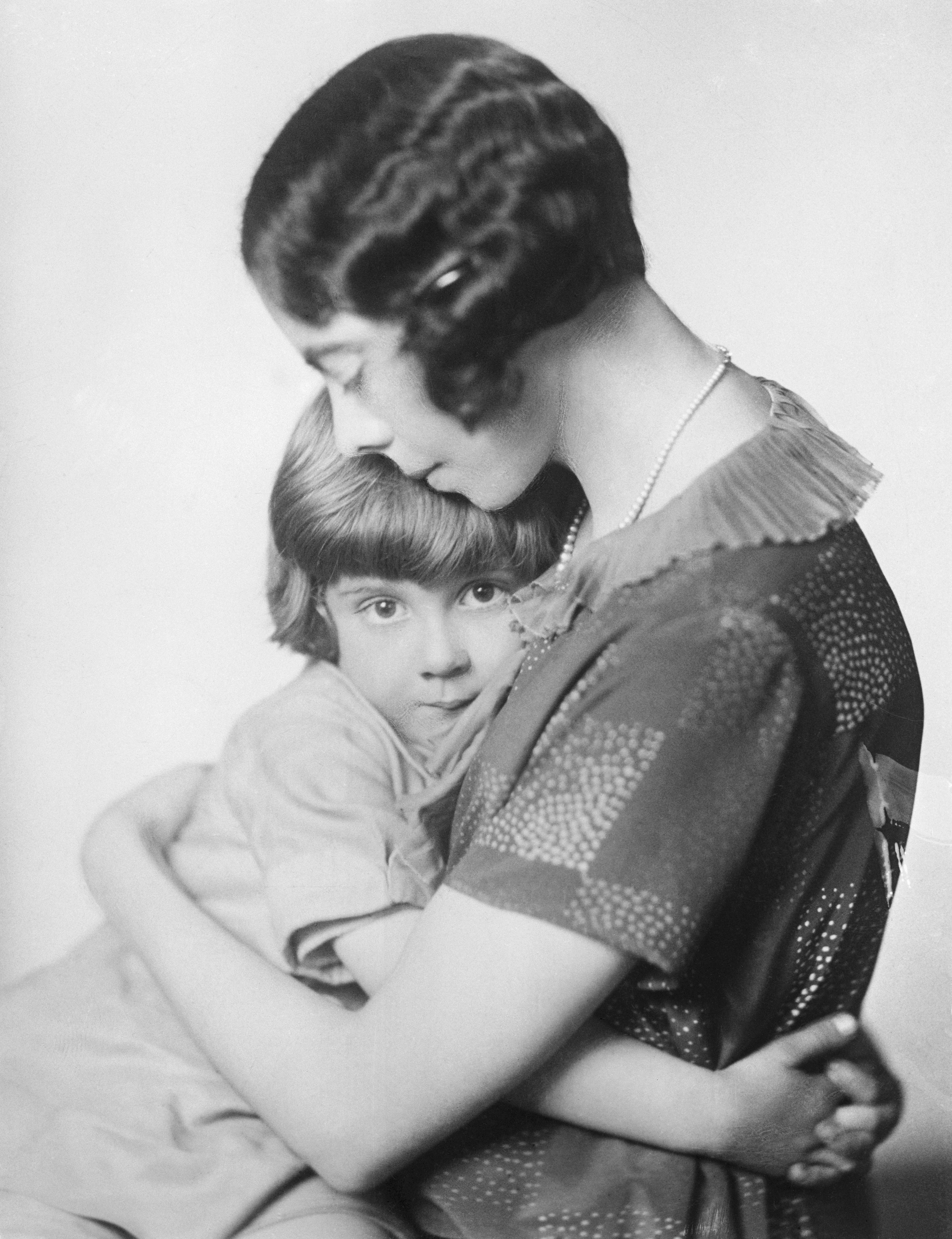 A vintage photo of a young child hugging an adult, who wears a patterned dress with a ruffled collar, displaying a tender and protective moment