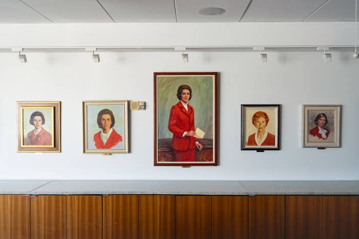 Portraits of women in red suits are displayed on a wall, each framed and centered above a wooden surface