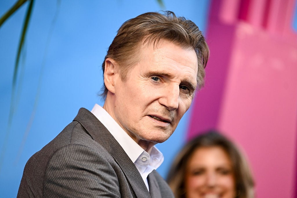 Liam Neeson, in a suit, poses at an event