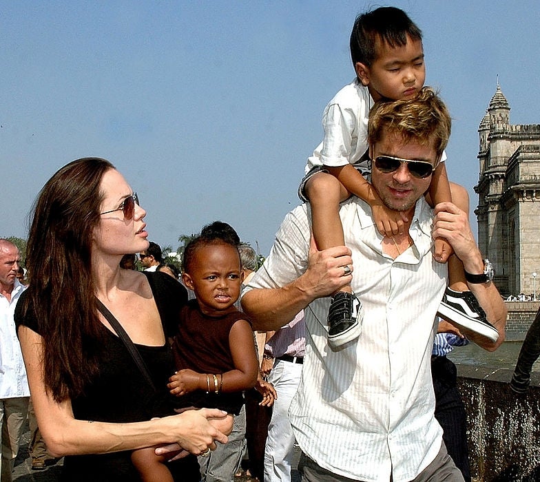 Angelina Jolie and Brad Pitt walk holding two of their kids outdoors