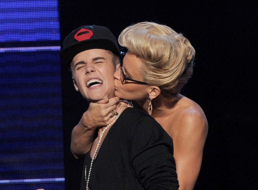 Two people on stage; one playfully kisses the other on the cheek