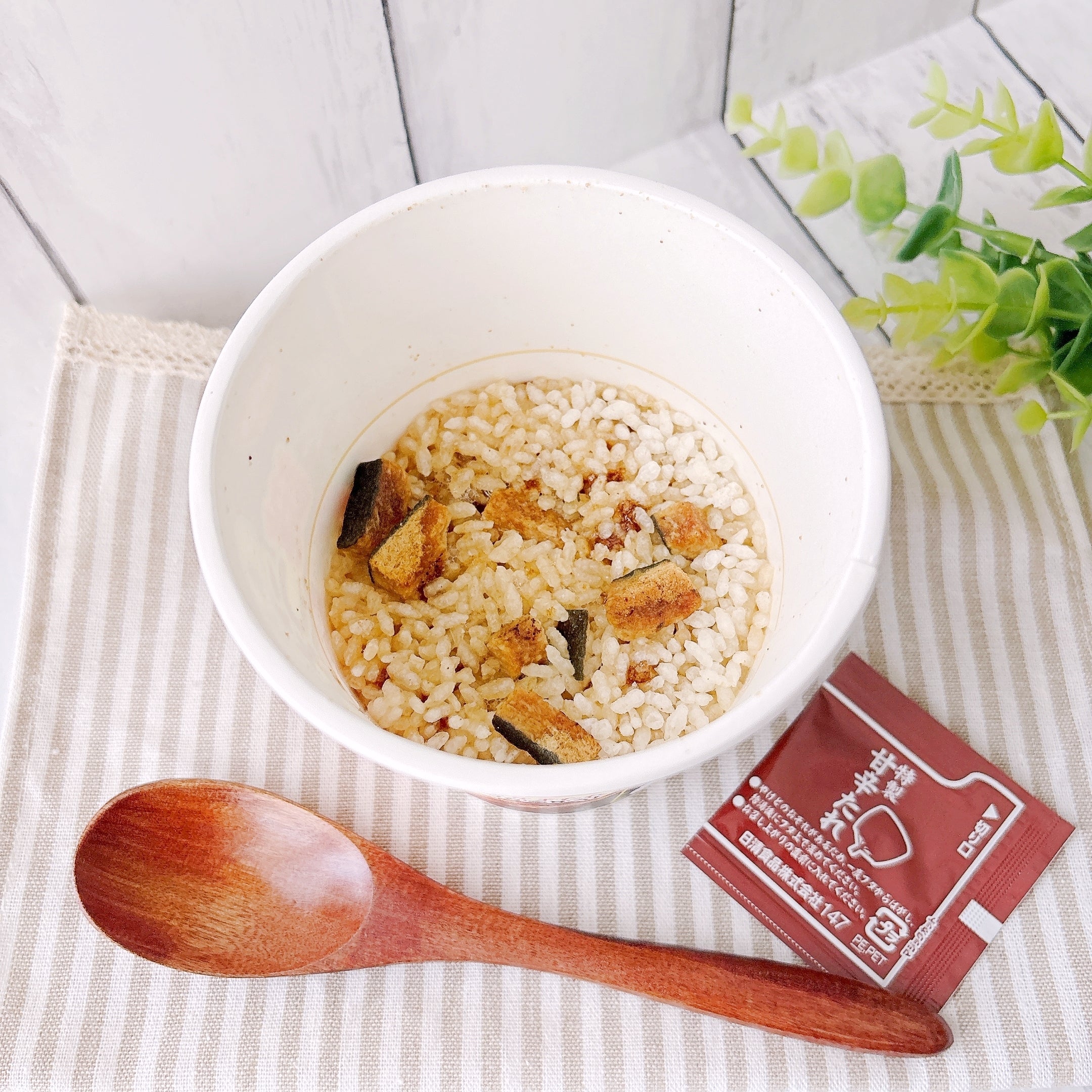 セブン‐イレブンで見つけた「日清謎うなぎ丼」カップと特製甘辛たれがテーブルの上に置かれている様子。