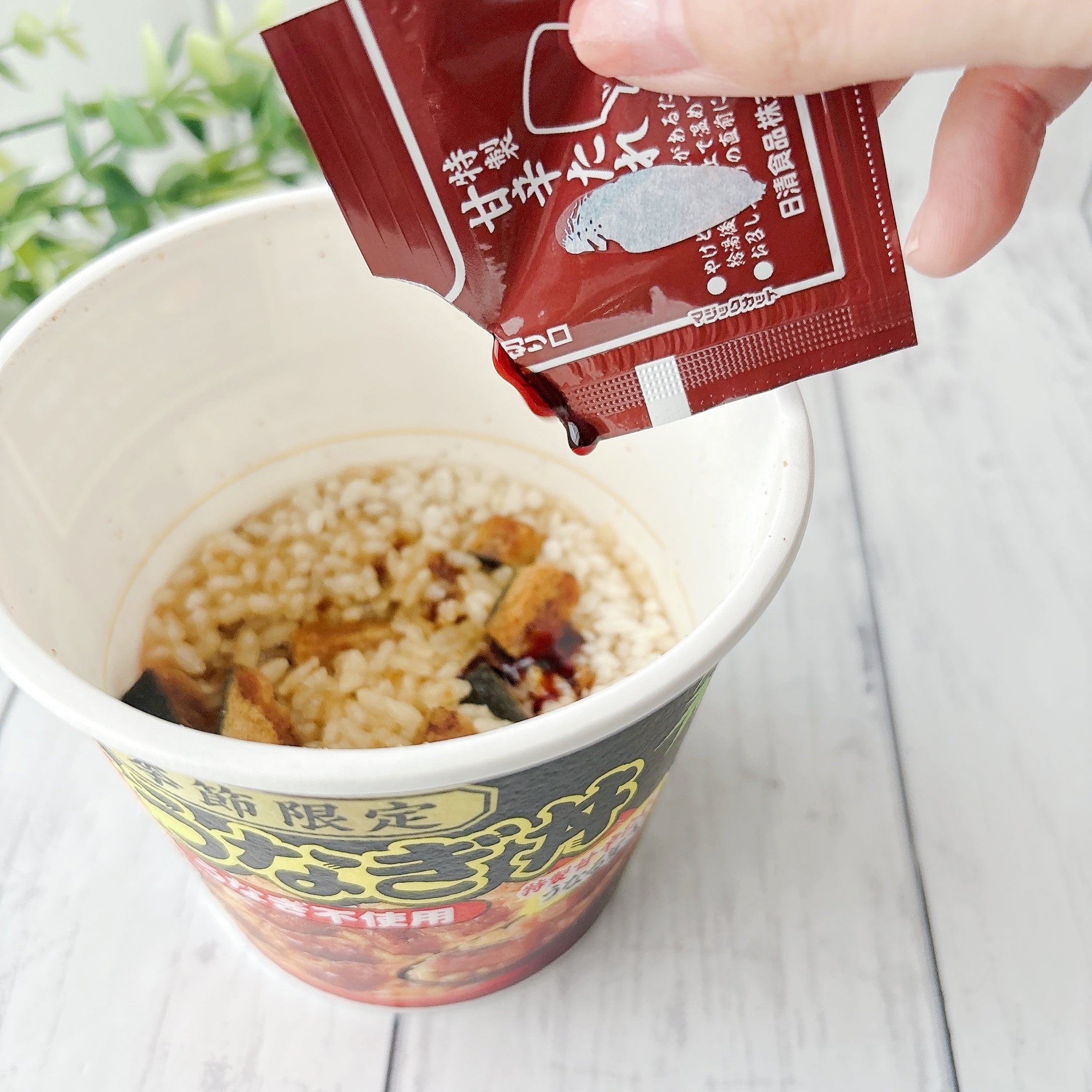 セブン‐イレブンで見つけた「日清謎うなぎ丼」容器入りのインスタント食品に、調味料を注いでいる様子。