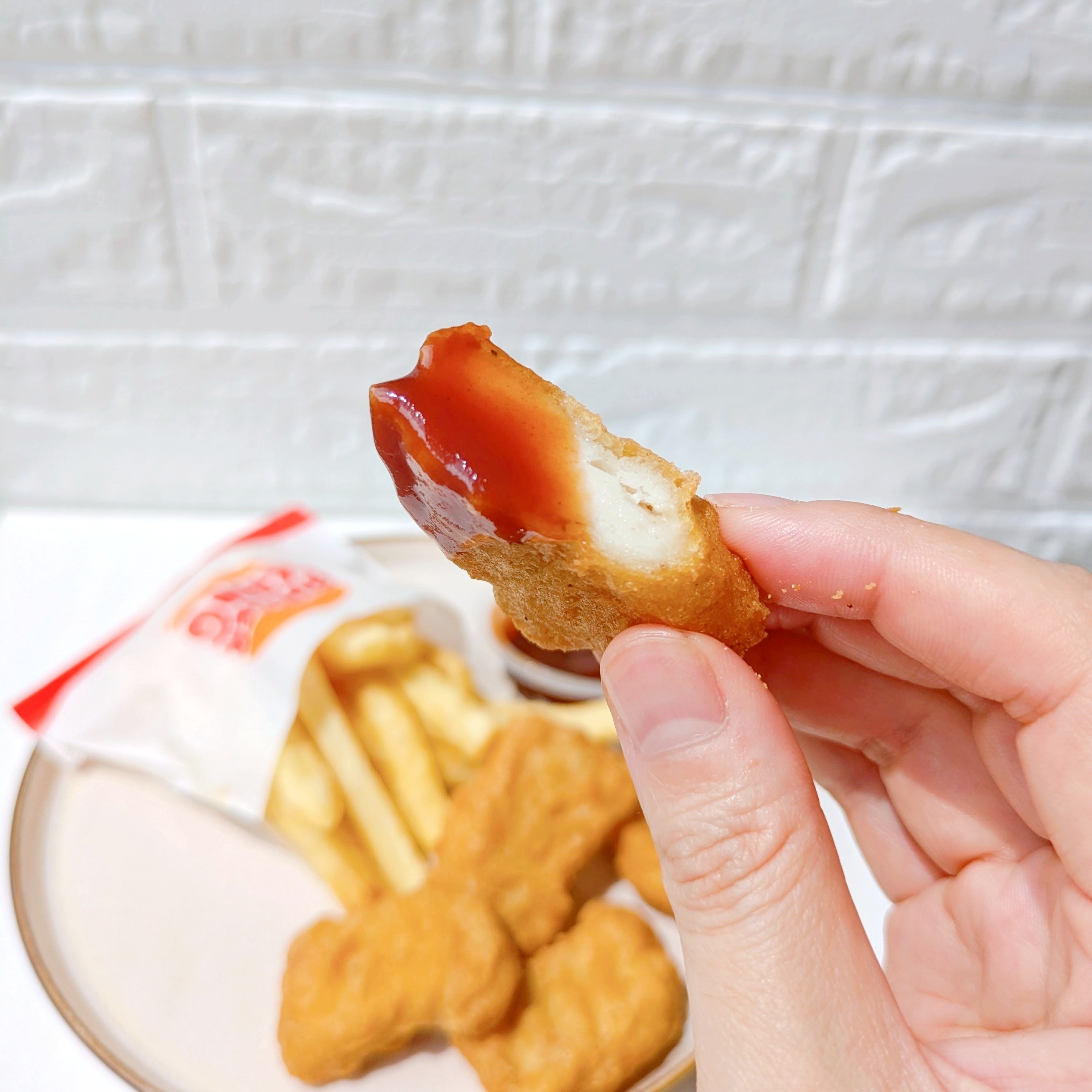 バーガーキングの「All DAY KING MEAL アボカドワッパーJr.」バーベキューソースをつけたチキンナゲットを持っており、背景にポテトフライが見える。