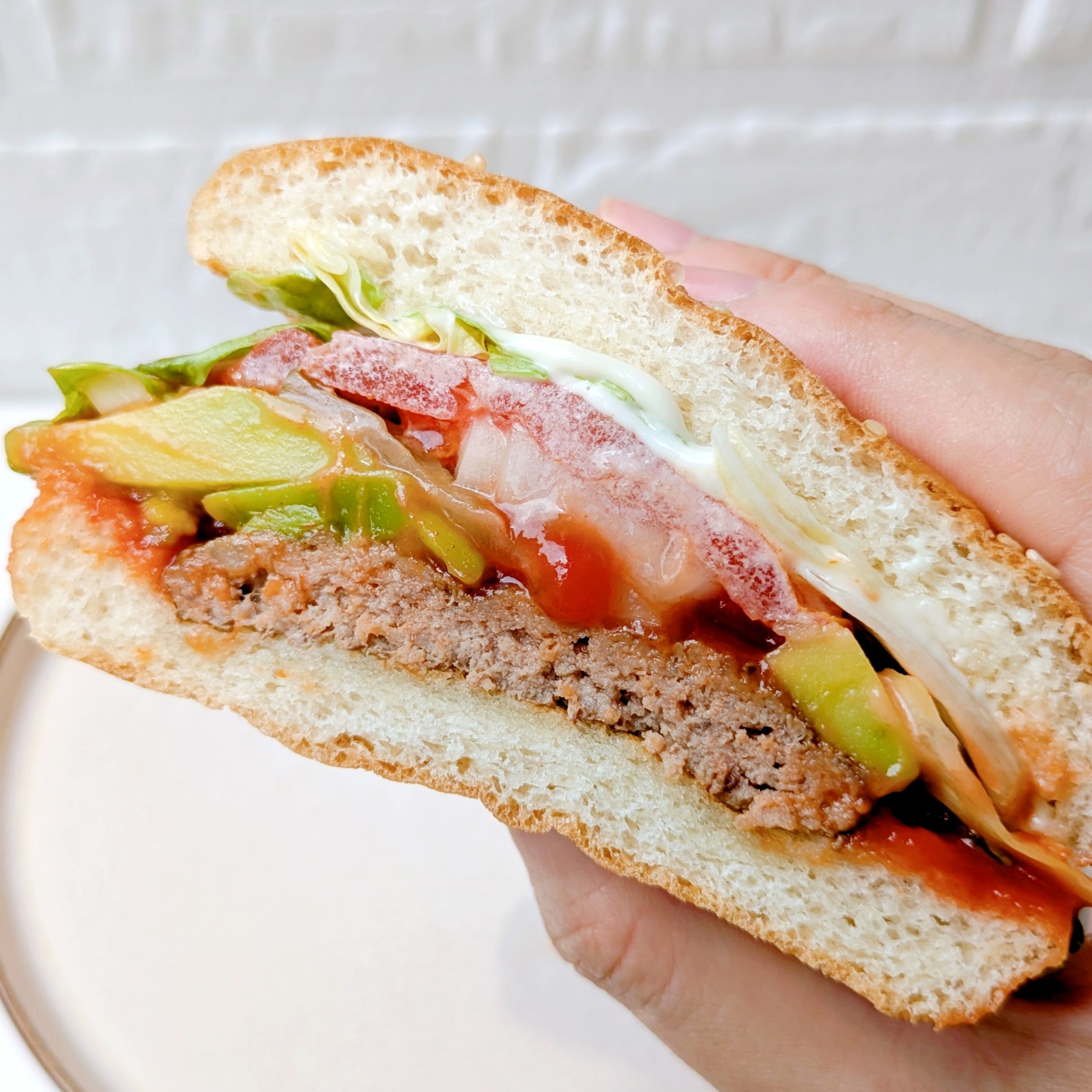 バーガーキングの「All DAY KING MEAL アボカドワッパーJr.」ハンバーガーの断面を手で持っている。レタス、トマト、パティ、アボカドが見える。