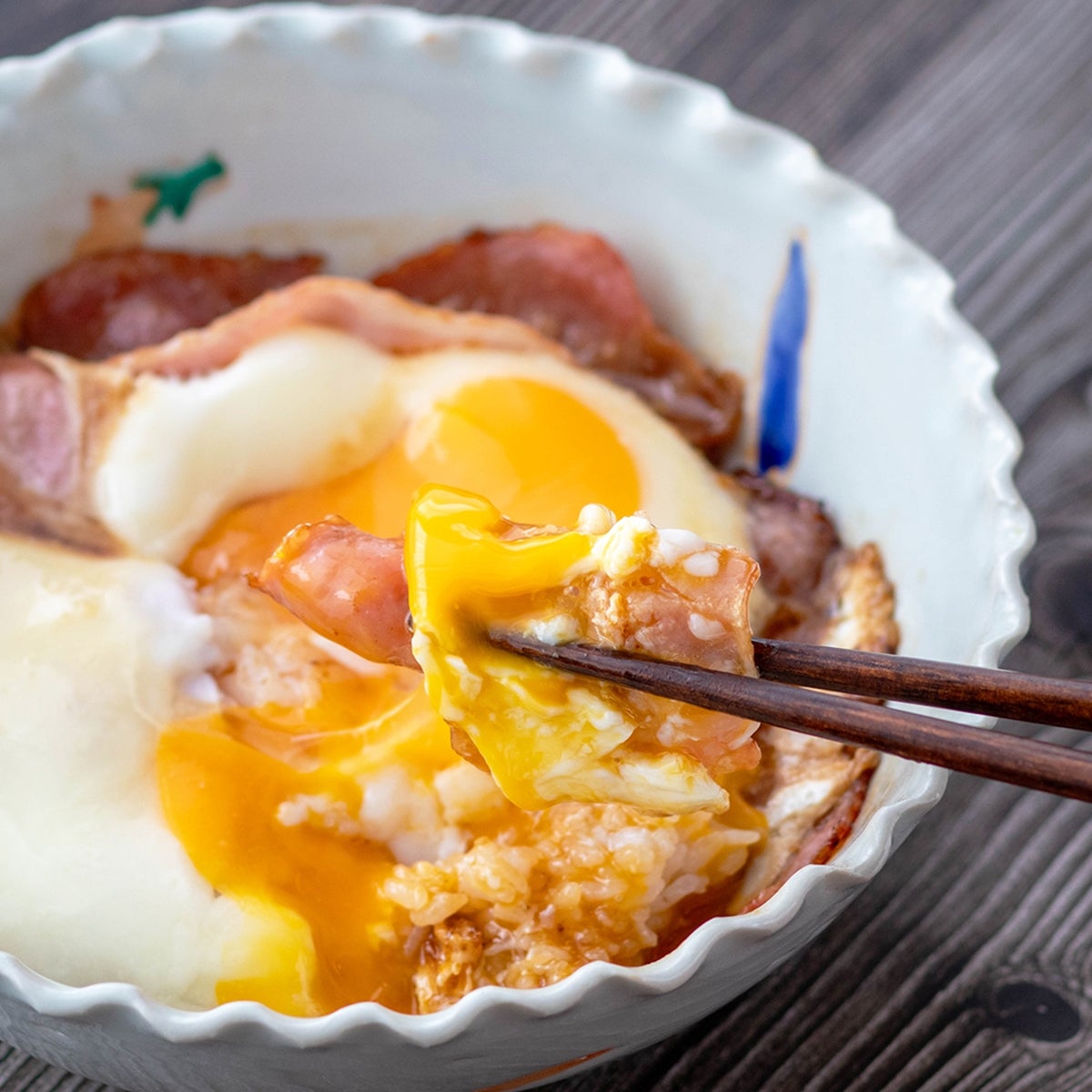 半熟卵がのったご飯を箸で持ち上げている様子。魅力的な朝食の一例。