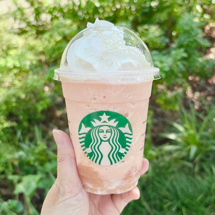 スターバックスのフラペチーノを持つ様子。背景は緑豊かな景色。